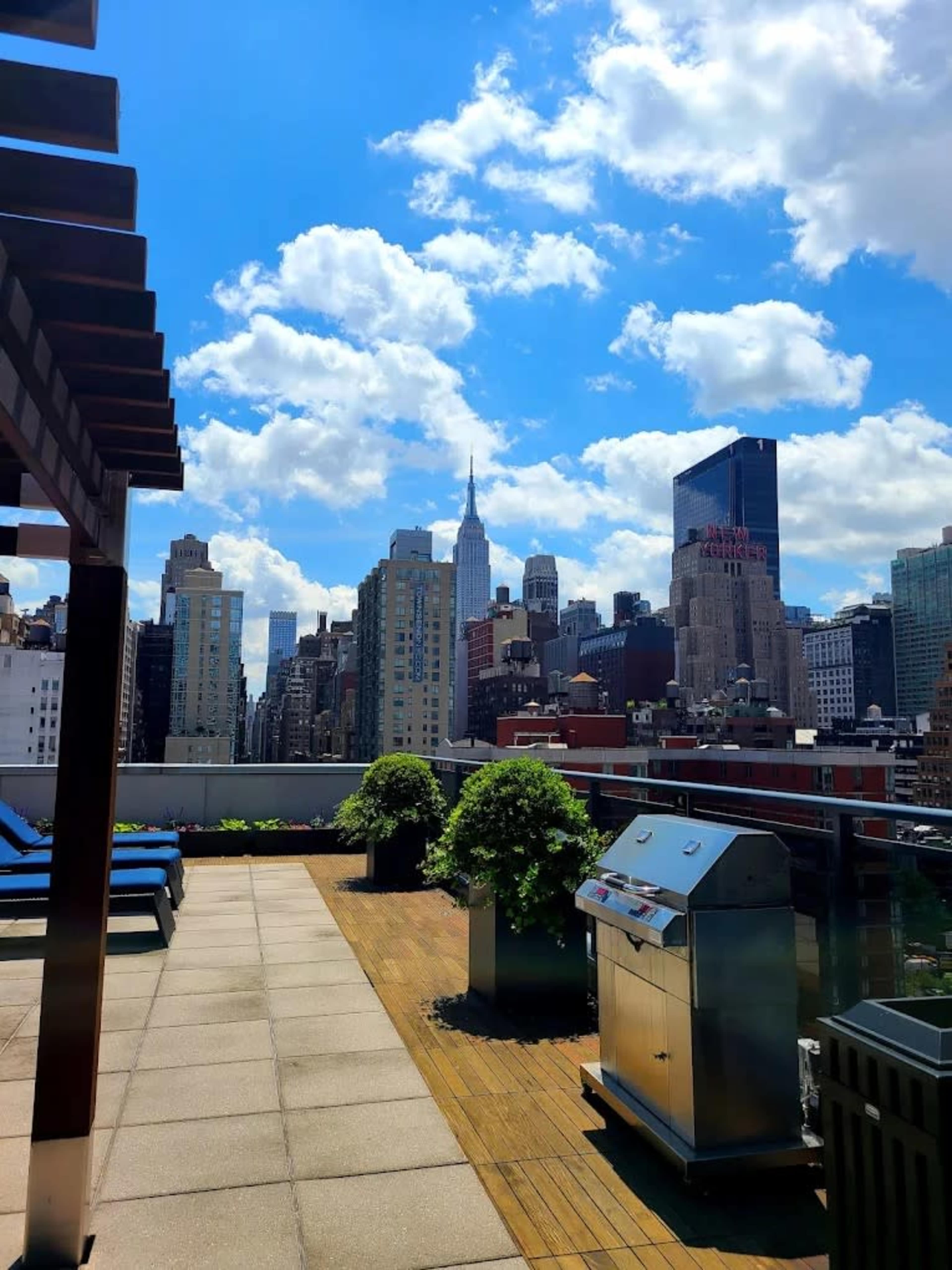 The image shows a rooftop view of a city skyline with the Empire State Building visible, under a partly cloudy blue sky.
