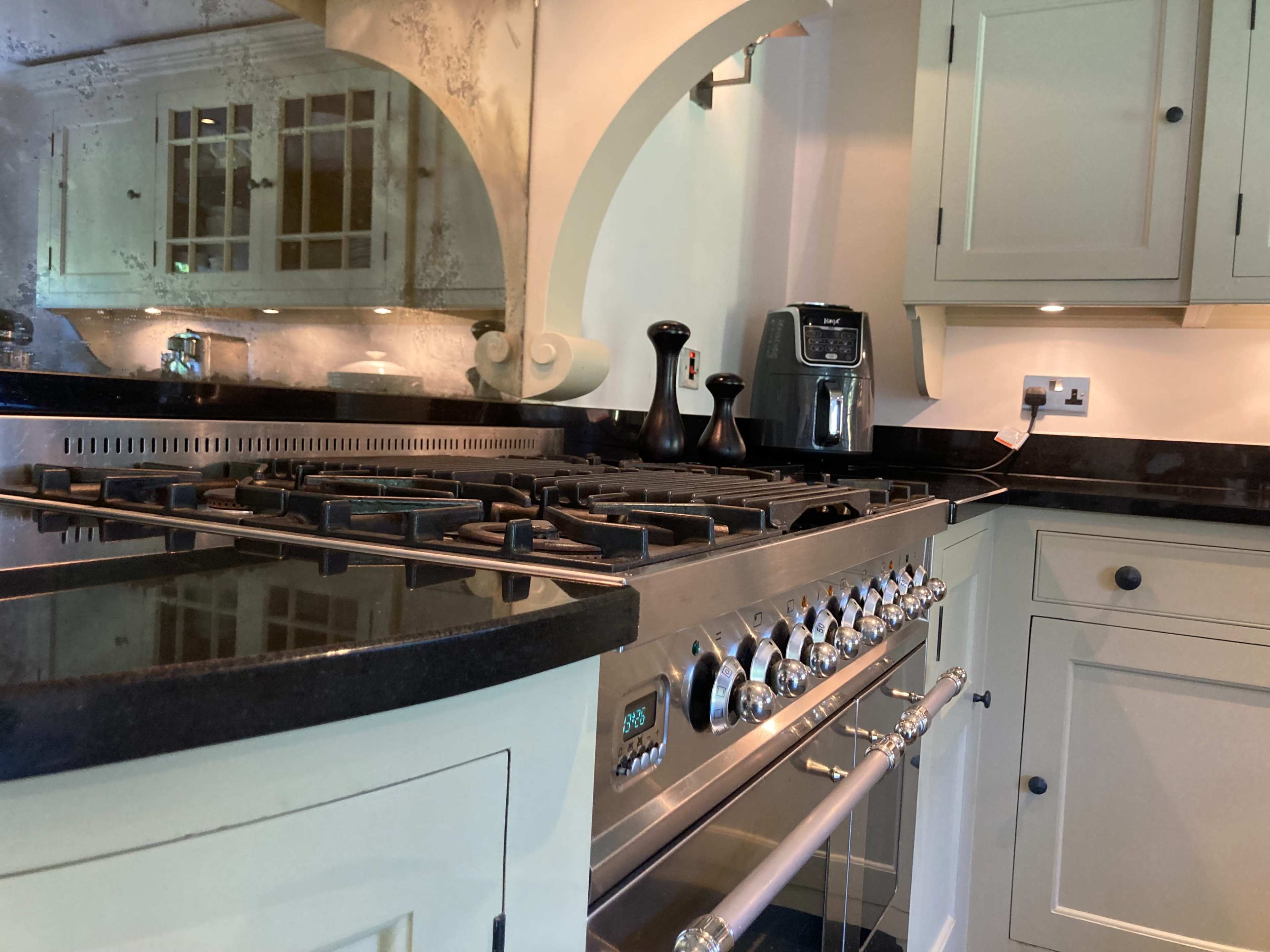 A stainless steel gas range with multiple burners, set against a backdrop of cream-colored cabinetry and a black granite countertop in a kitchen.