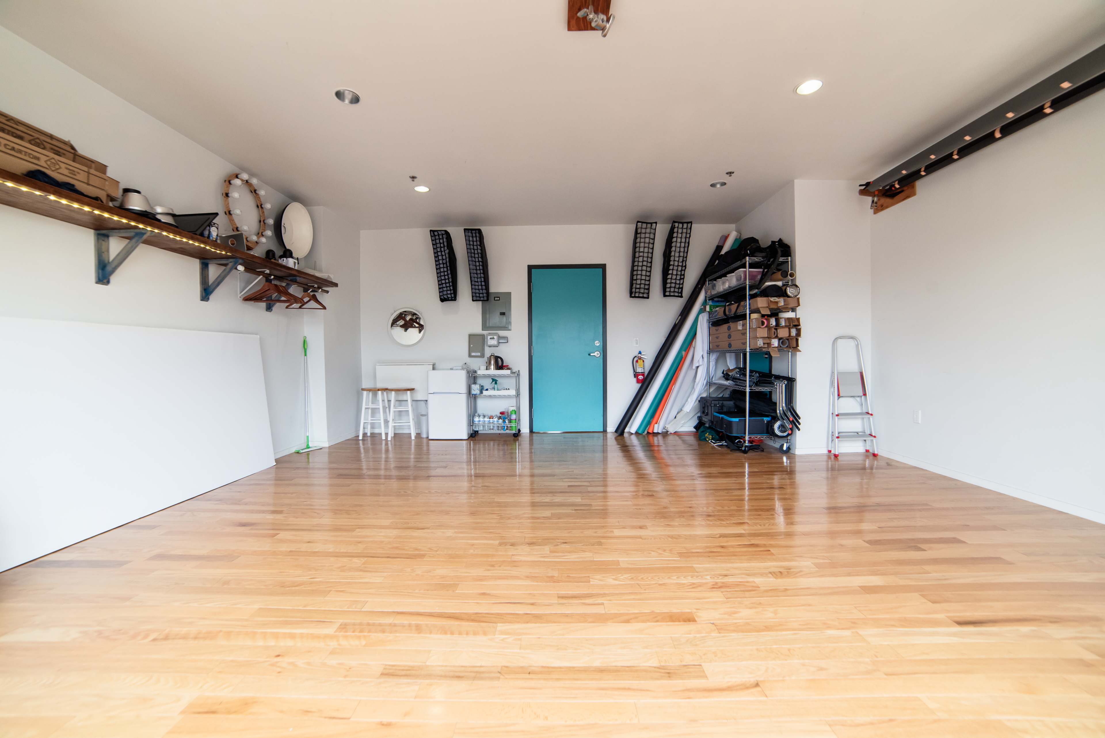 A spacious room with wooden flooring, shelves storing various items, a small kitchenette area, and a blue door.