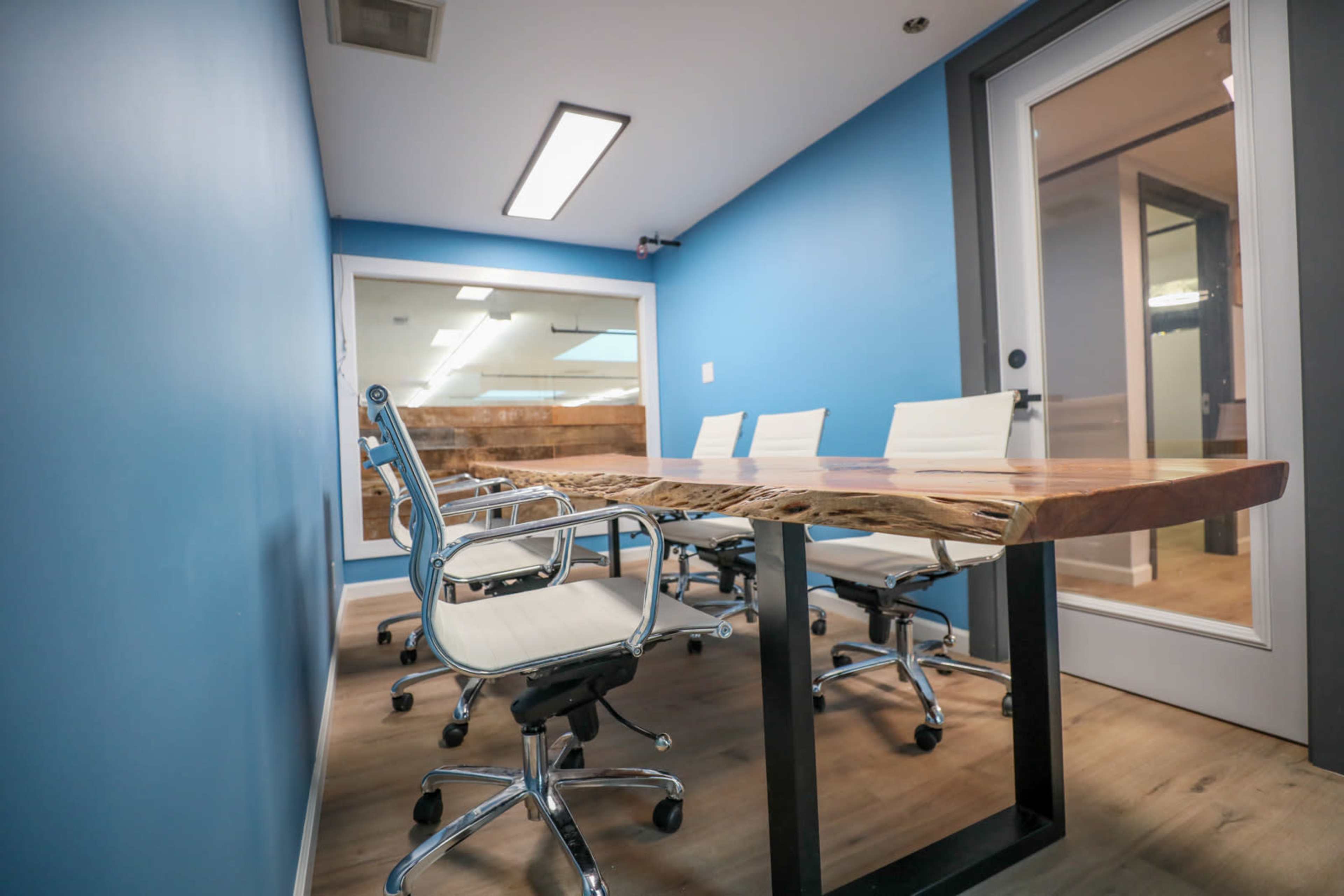 A modern conference room features a wooden table and ergonomic white chairs against a blue wall.