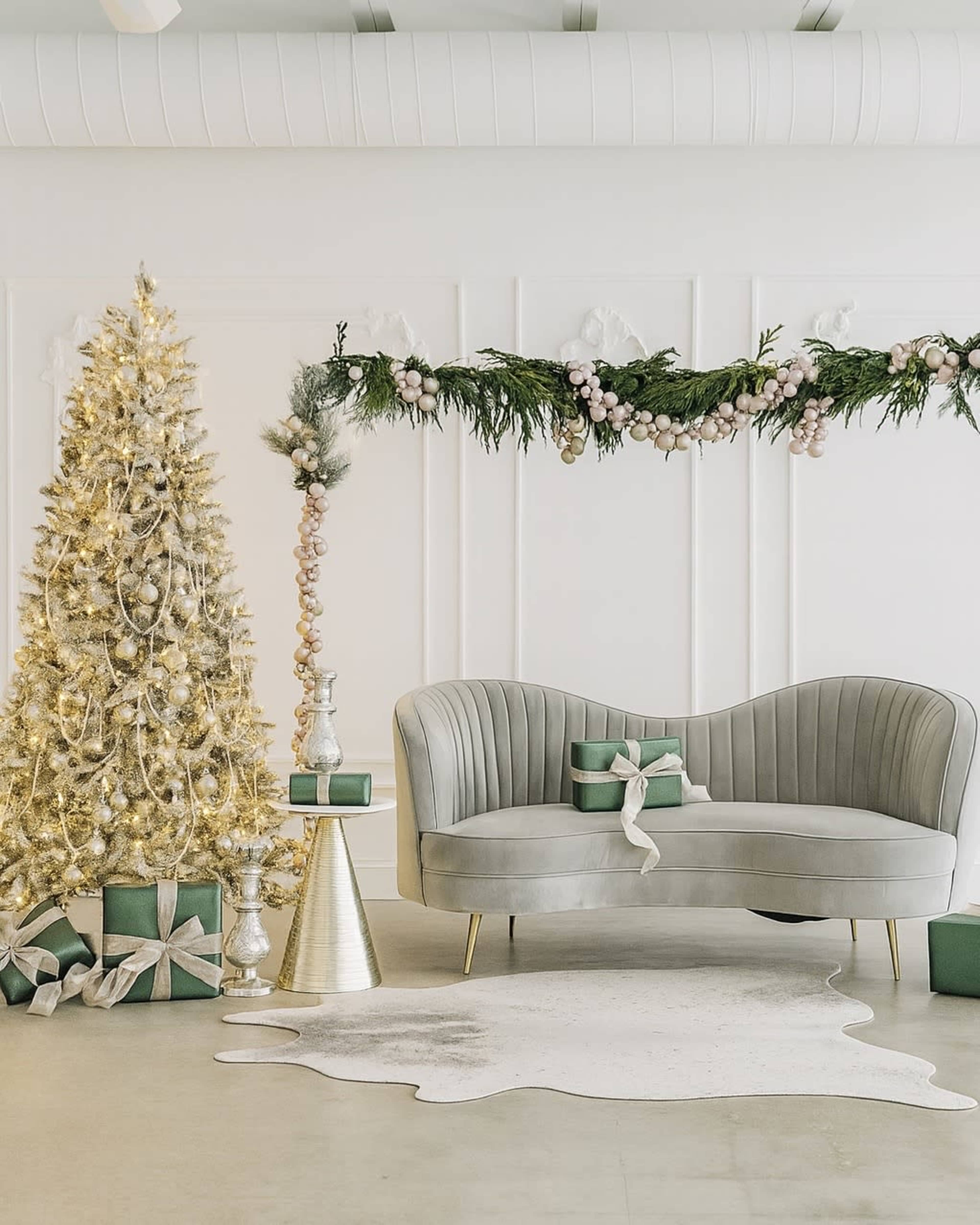 The image features a stylish, modern living room decorated for the holidays with a lit Christmas tree, gifts, and a curved gray sofa.