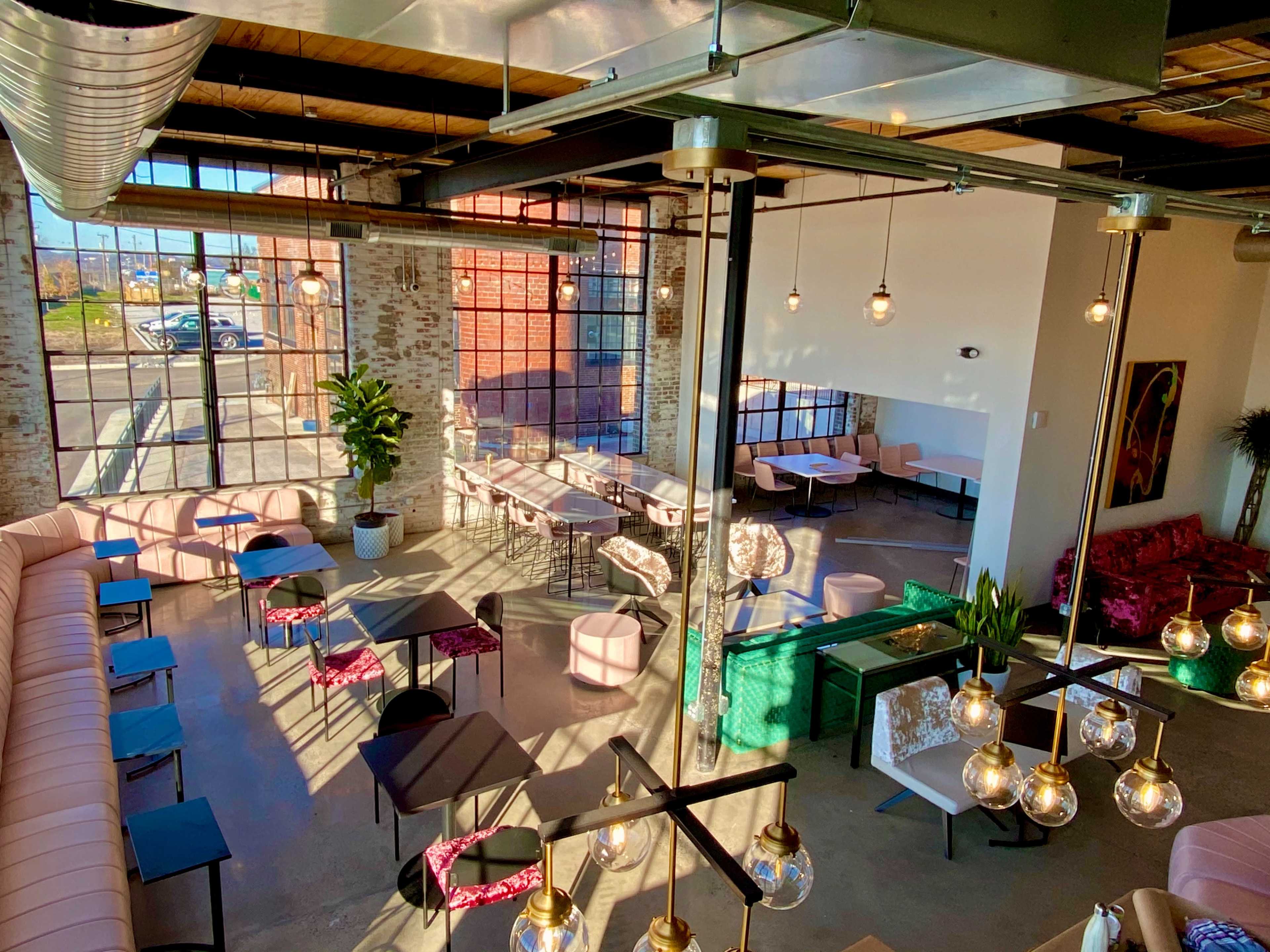 A spacious cafe with large windows, modern furniture, and various seating arrangements.