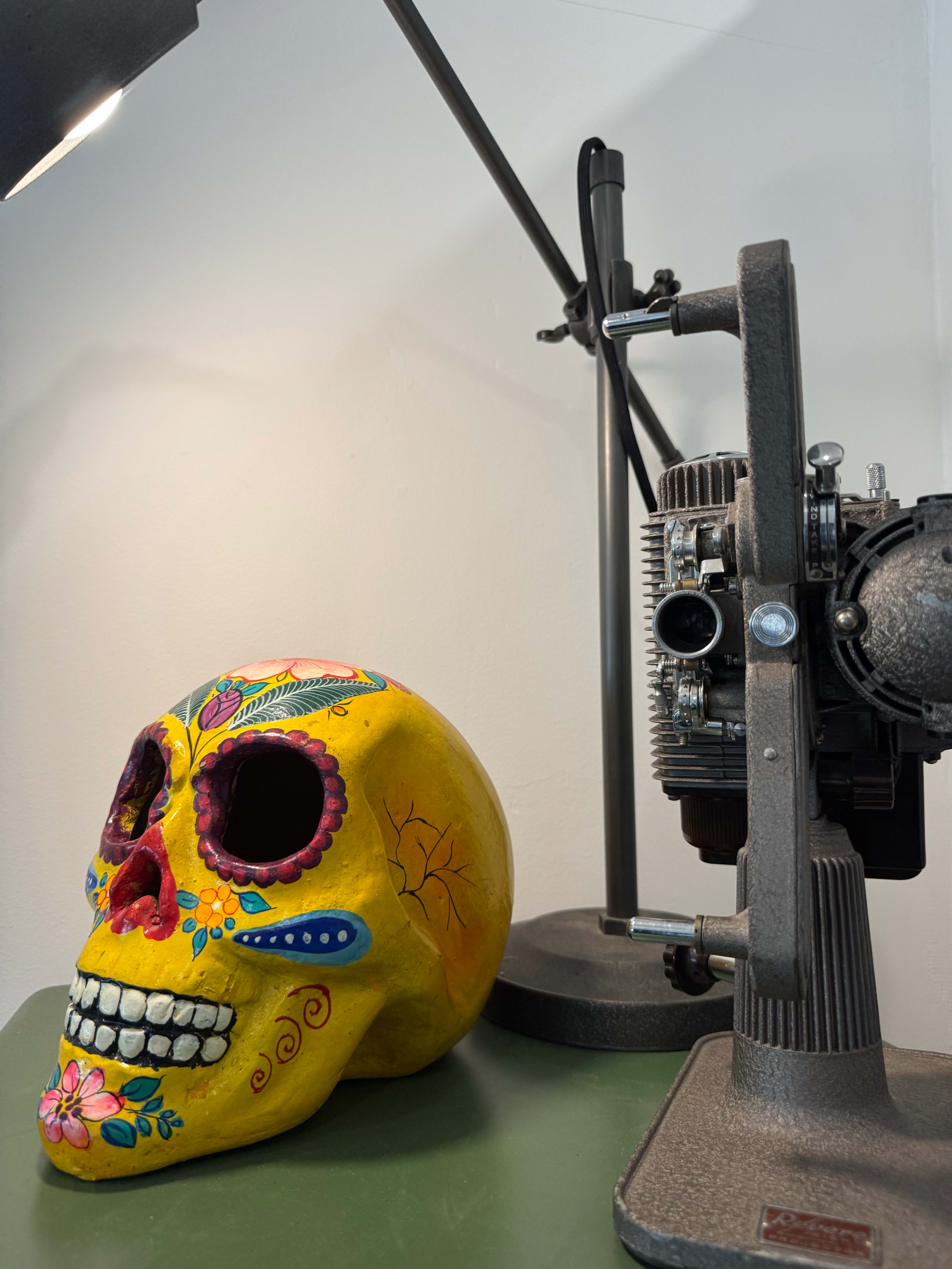 The image shows a colorful decorative skull beside a vintage sewing machine on a green table.