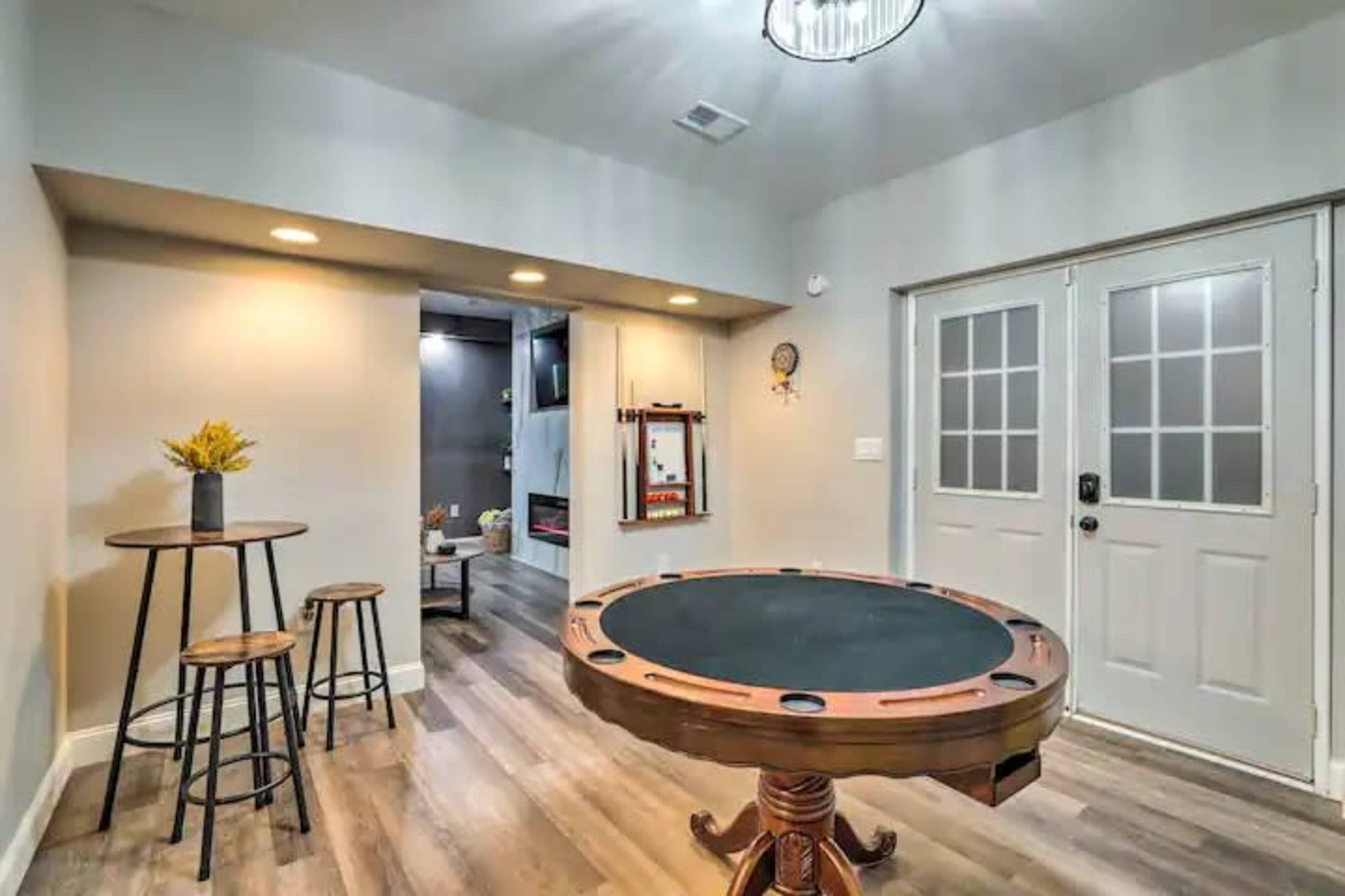 A room featuring a round poker table with a green felt surface, two tall bar stools, and a set of double doors leading outside.