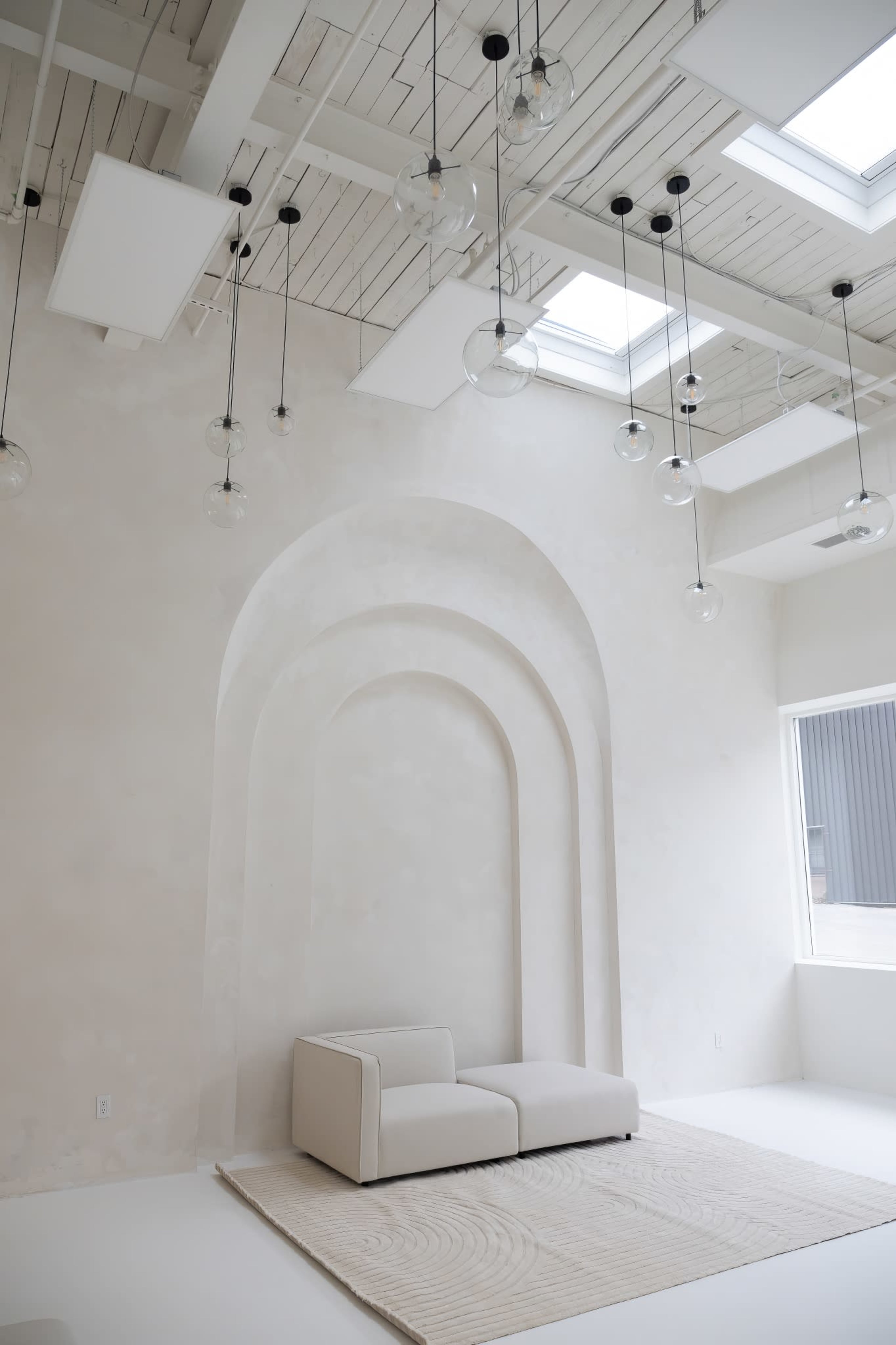 A minimalist interior featuring a light-colored wall with arched alcoves and a small sofa on a textured rug.