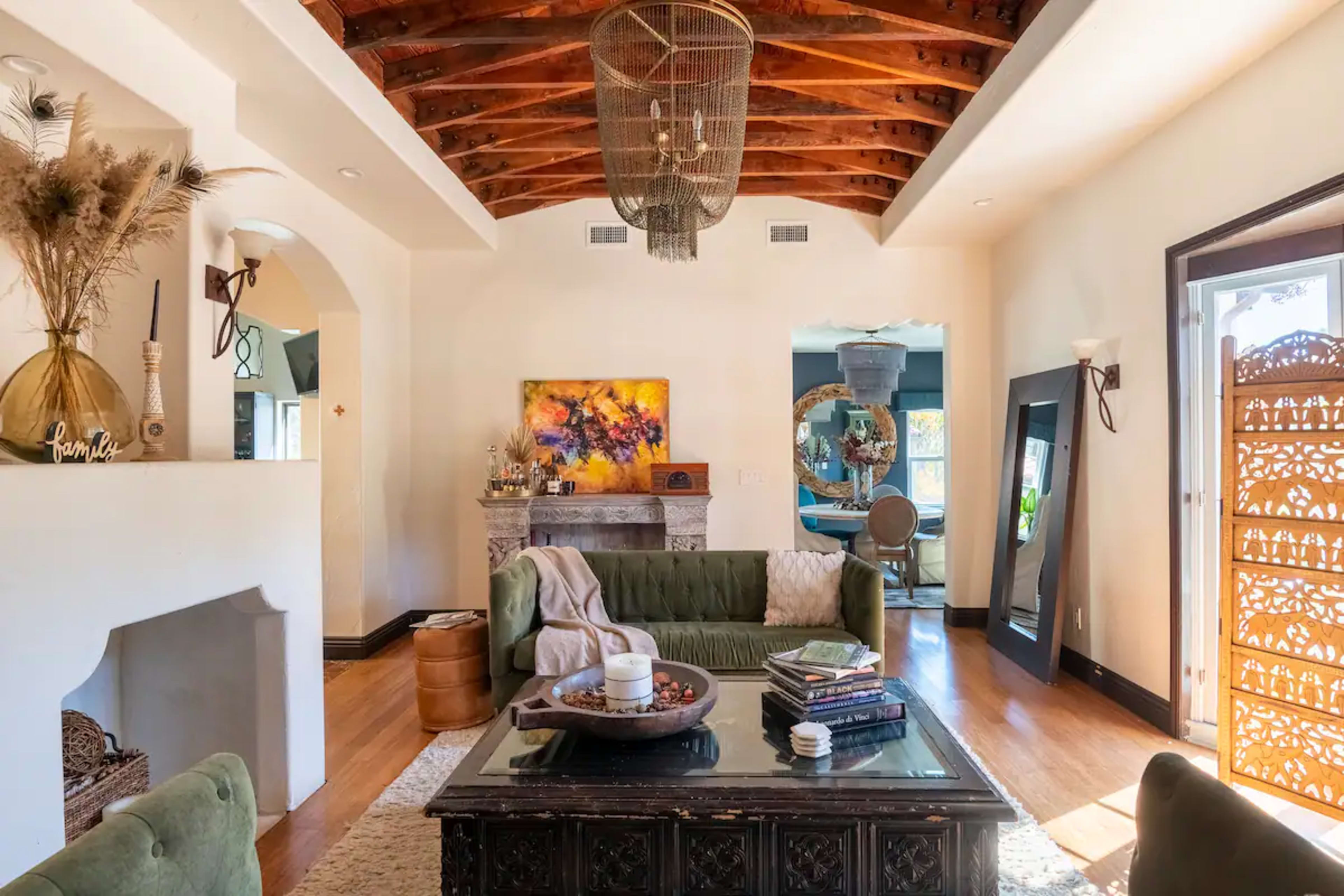 A living room with a green sofa, wooden ceiling beams, and a decorative fireplace, accented by various decorative elements and soft lighting.