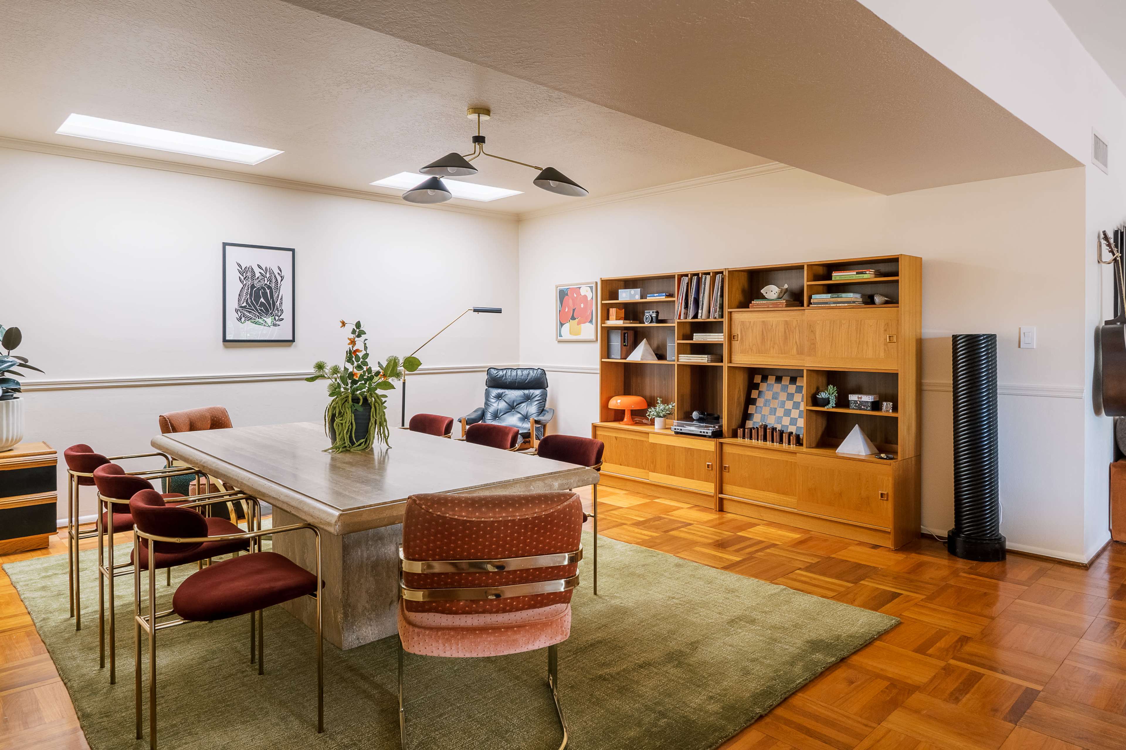 A spacious dining area features a wooden table surrounded by burgundy chairs, with a bookshelf and decorative elements on display along the wall.