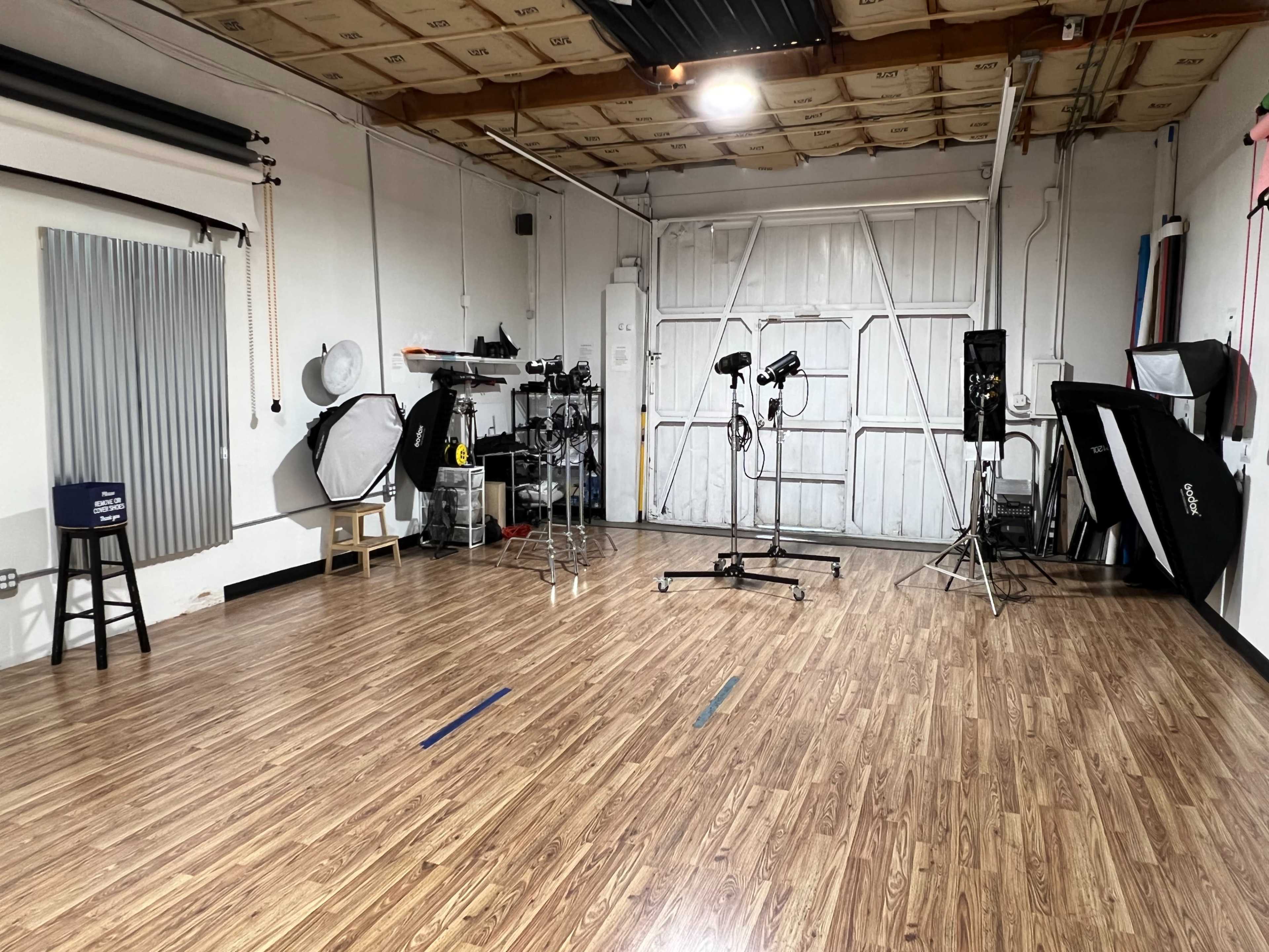 A photography studio with wooden floors, various lighting equipment, and a large roll-up door at the back.