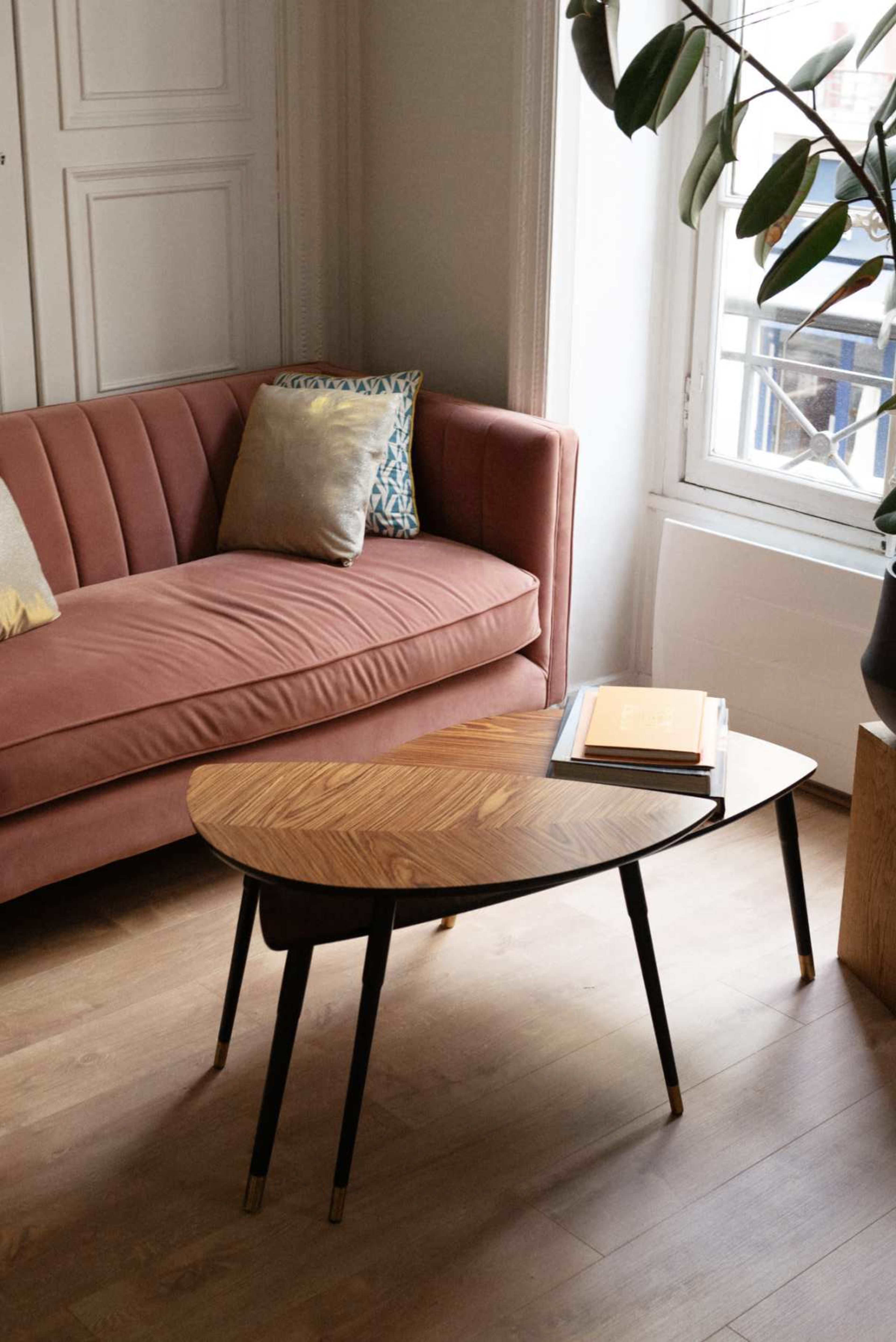 A mid-century modern living room features a pink couch with decorative pillows, a wooden coffee table, and a large window with natural light.