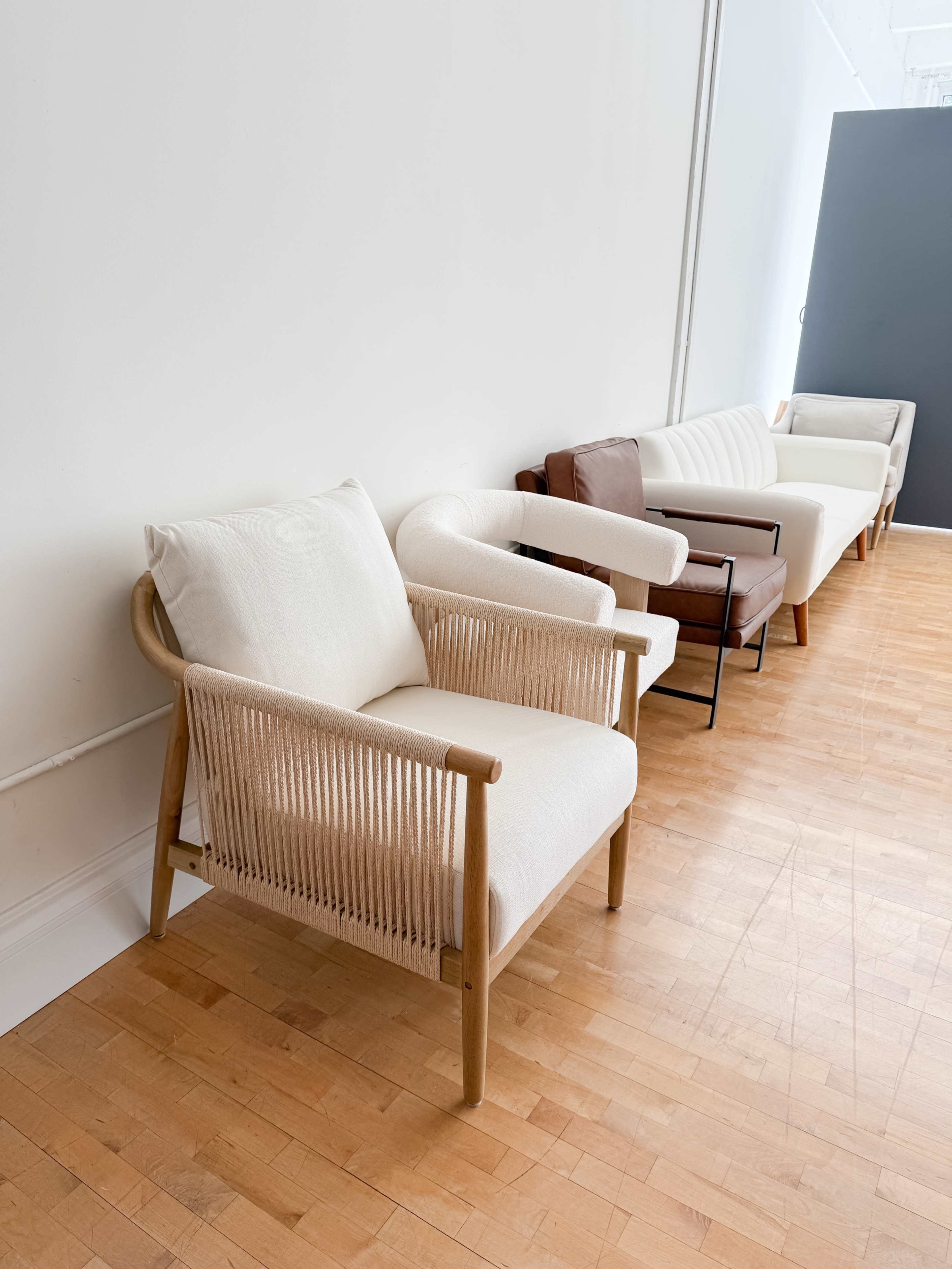 The image shows a row of various styled chairs positioned against a white wall in a minimalist interior space.