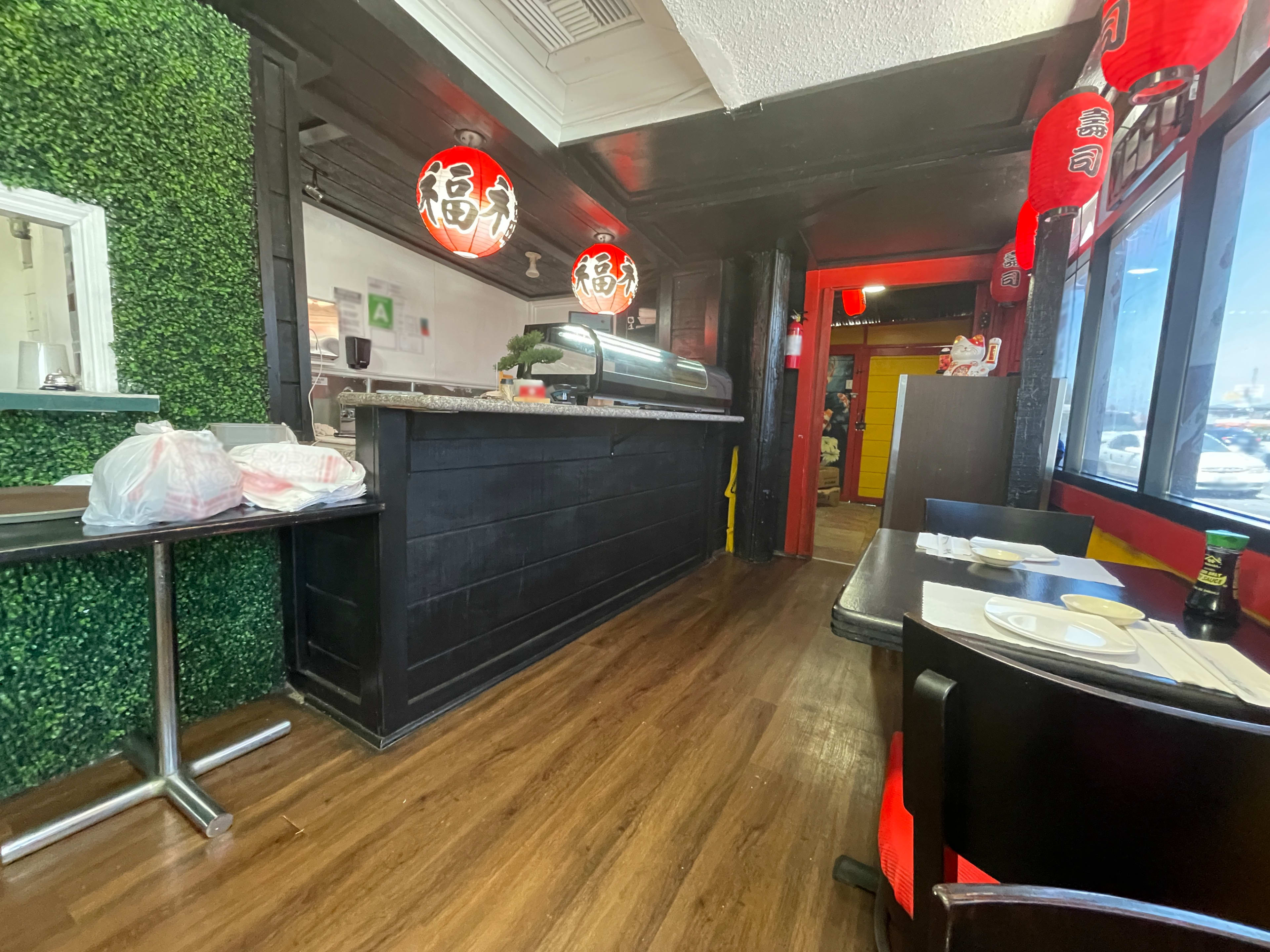 The image shows the interior of a restaurant featuring a sushi bar, wooden flooring, and green decor on the walls.
