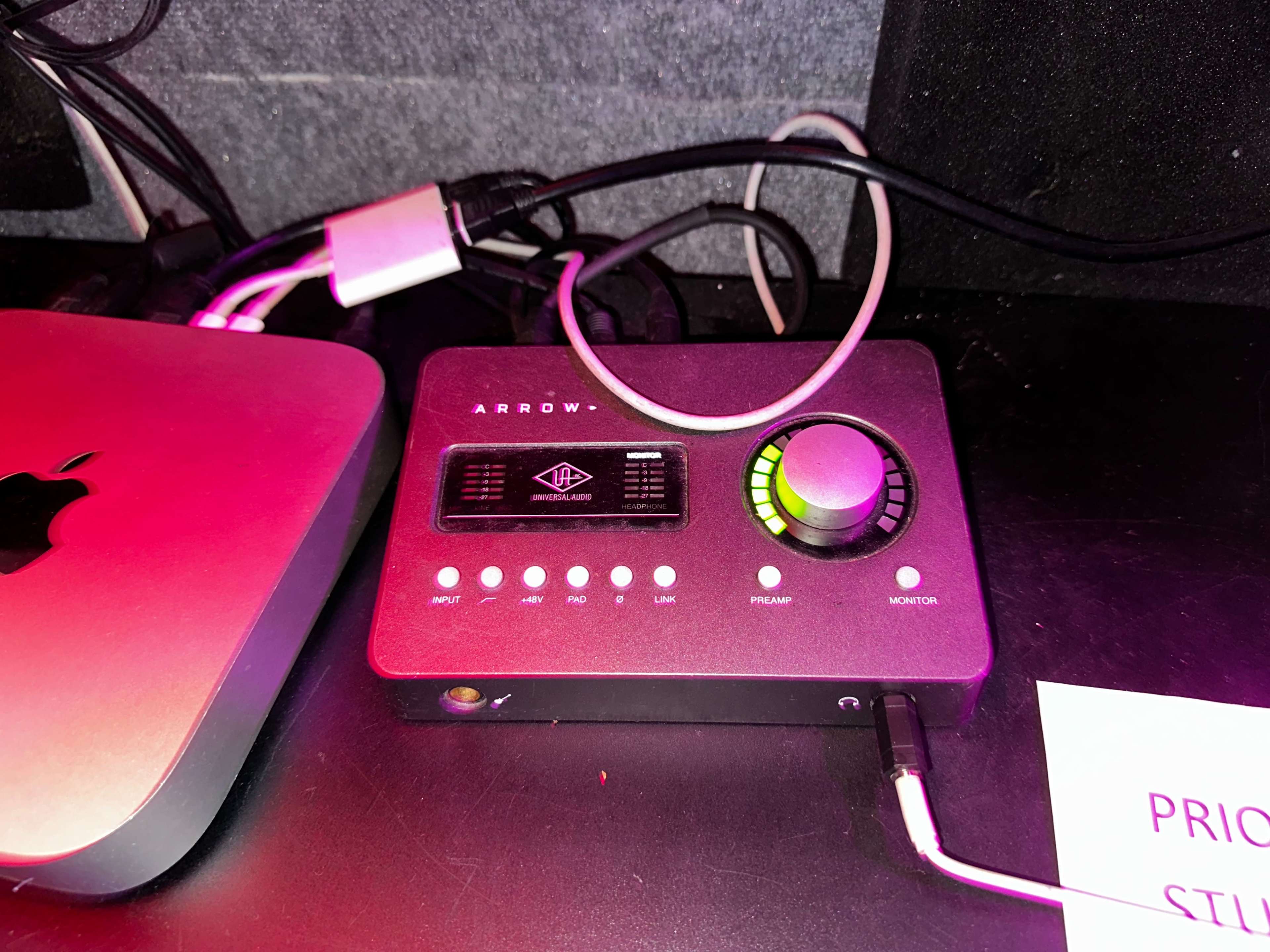 An audio interface labeled "ARROW" with various input/output ports and a volume control knob, placed next to a Mac computer.