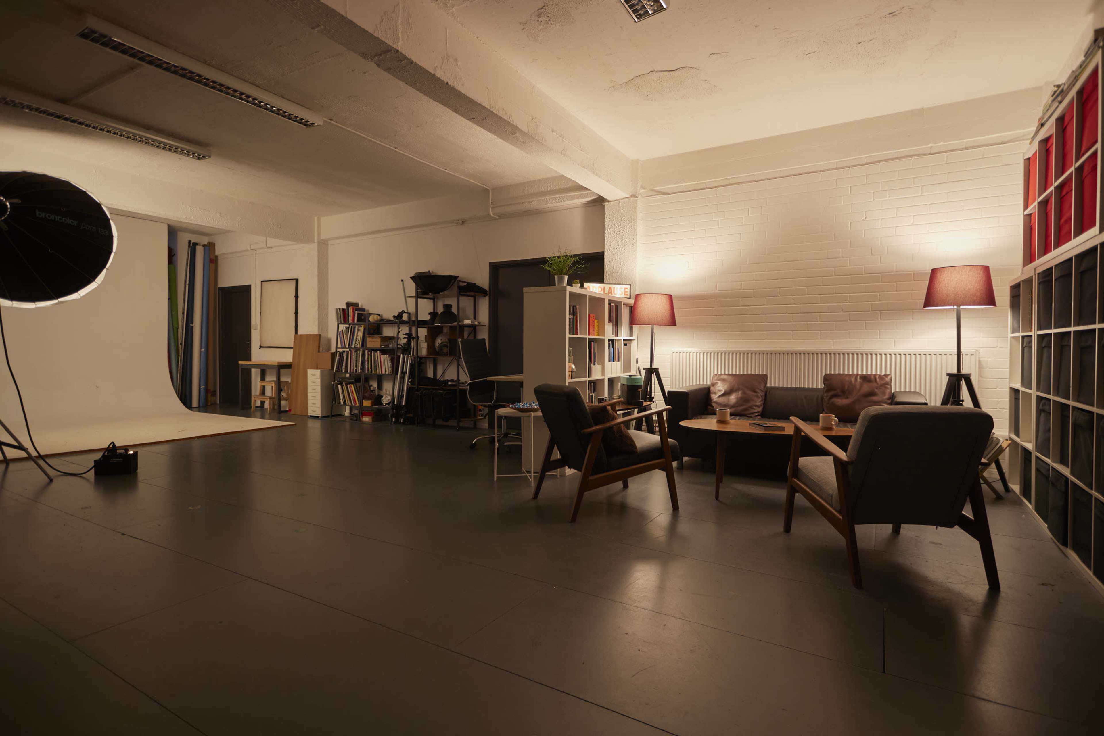 A spacious studio with wooden furniture, bookshelves, lamps, and a photography backdrop setup.