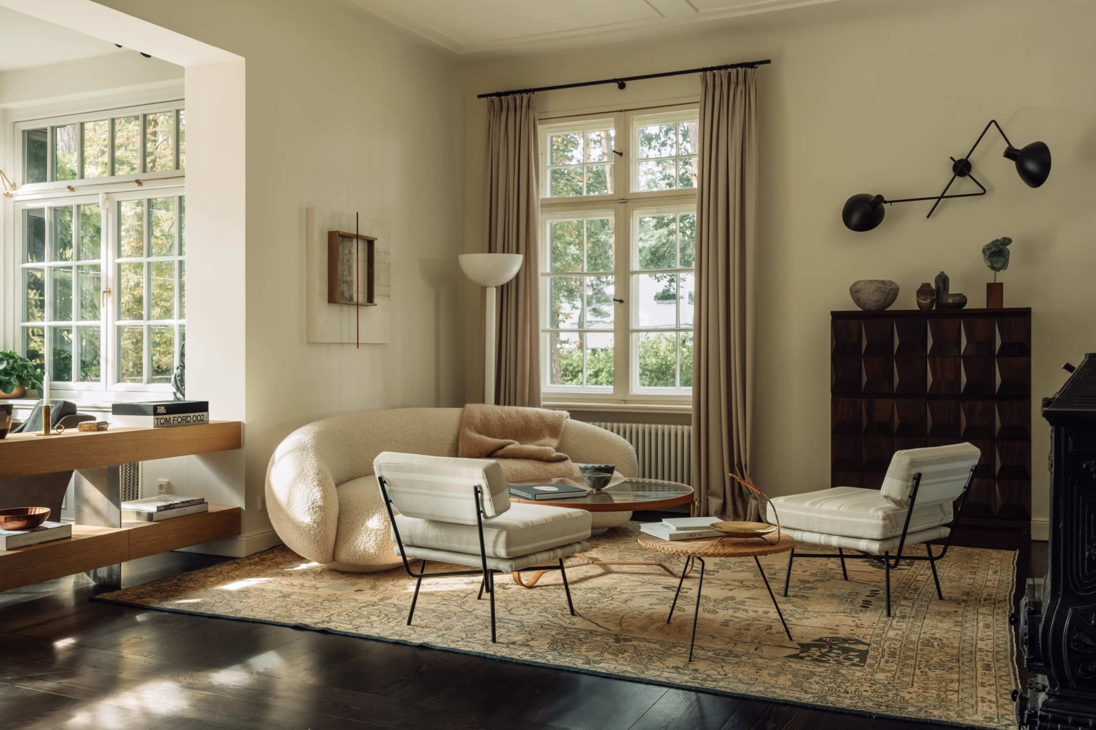 A modern living room with a curved sofa, two armchairs, a coffee table, and large windows allowing natural light to enter.