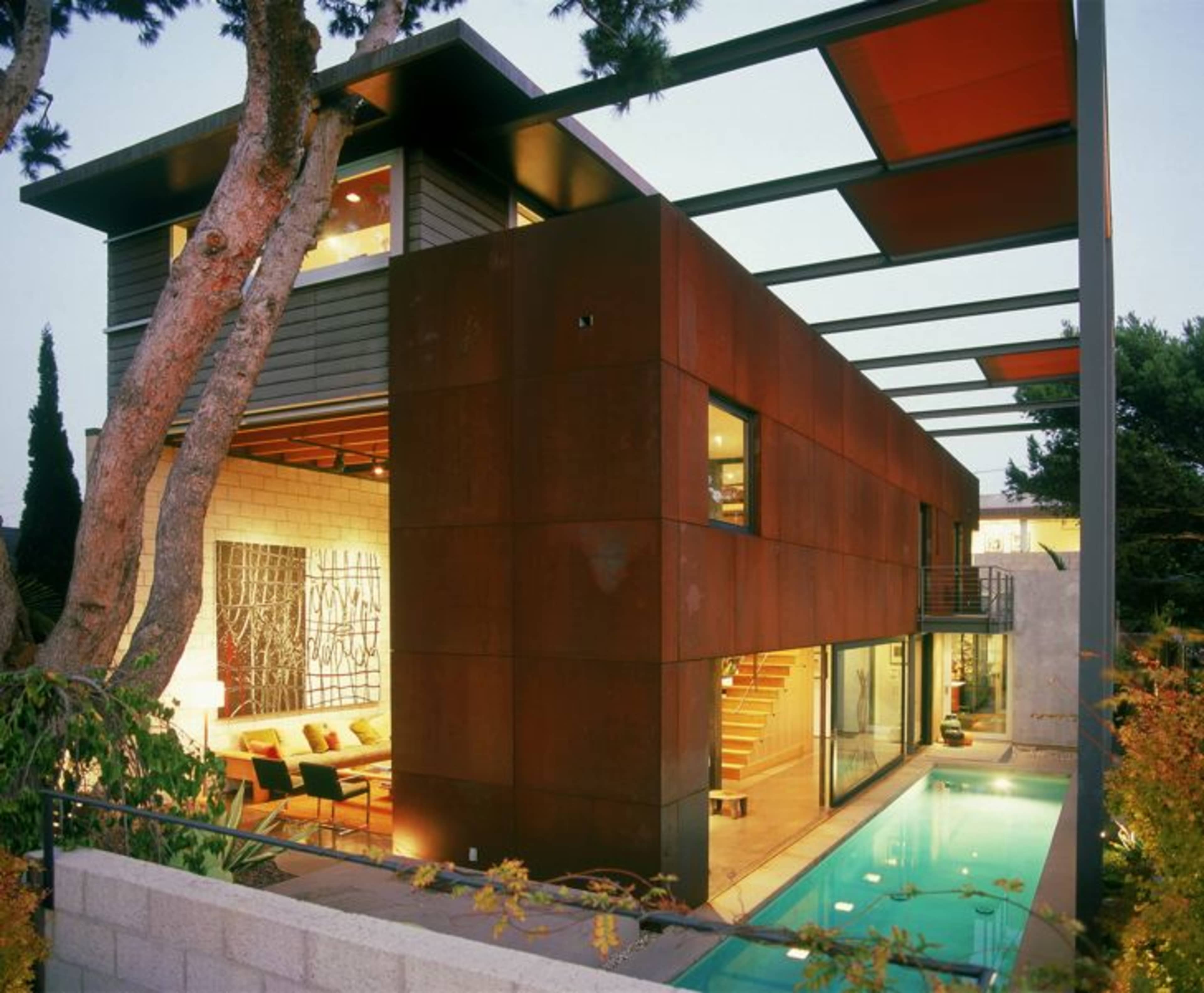 A modern house featuring a rust-colored exterior, large windows, and an outdoor pool, set amidst greenery and trees.