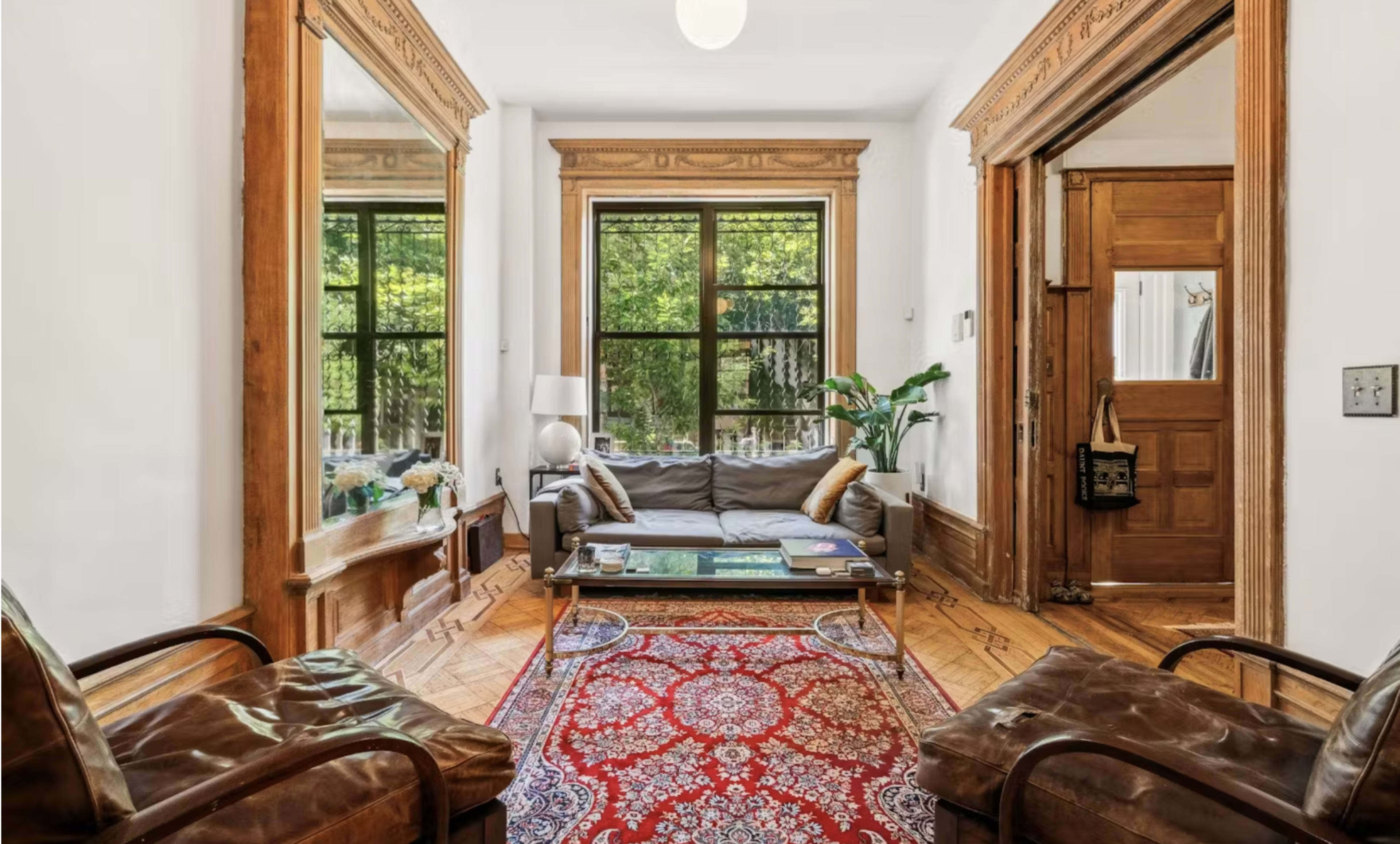 A living room with a sofa, two chairs, a coffee table, and large windows framed by wooden moldings.