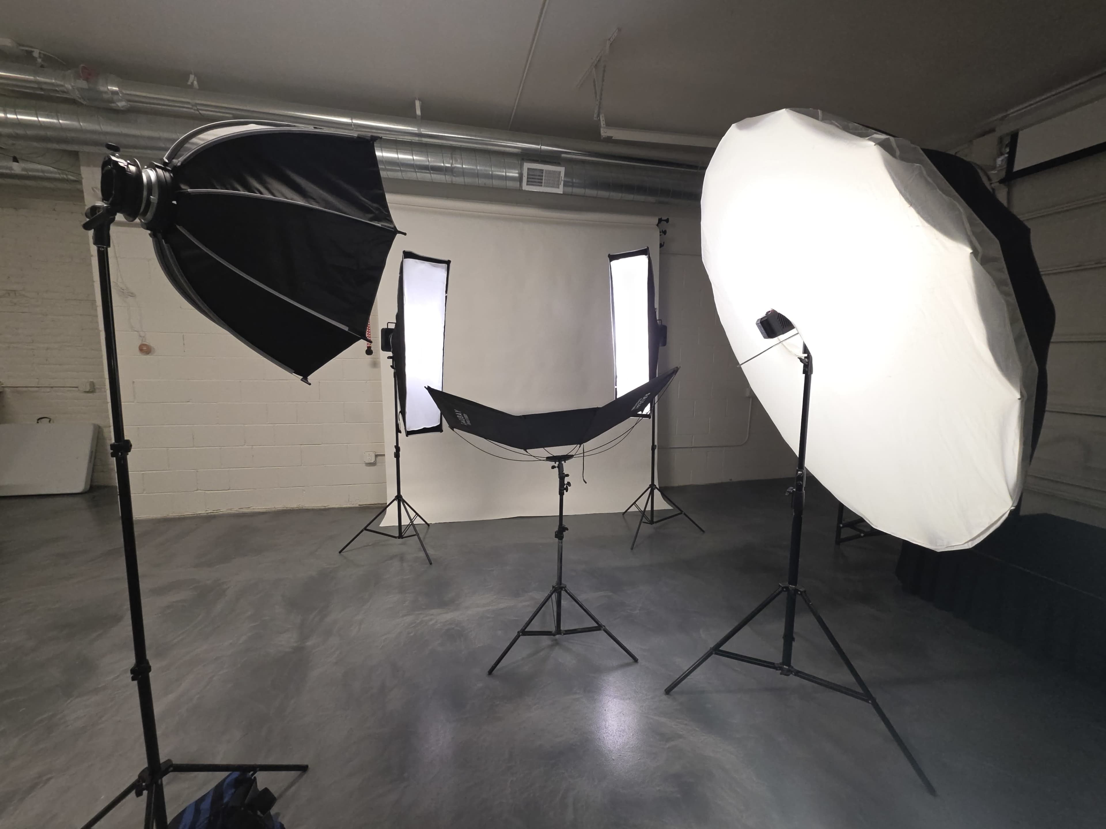 The image shows a photography studio setup with multiple light sources, including softboxes and umbrellas, arranged around a backdrop.