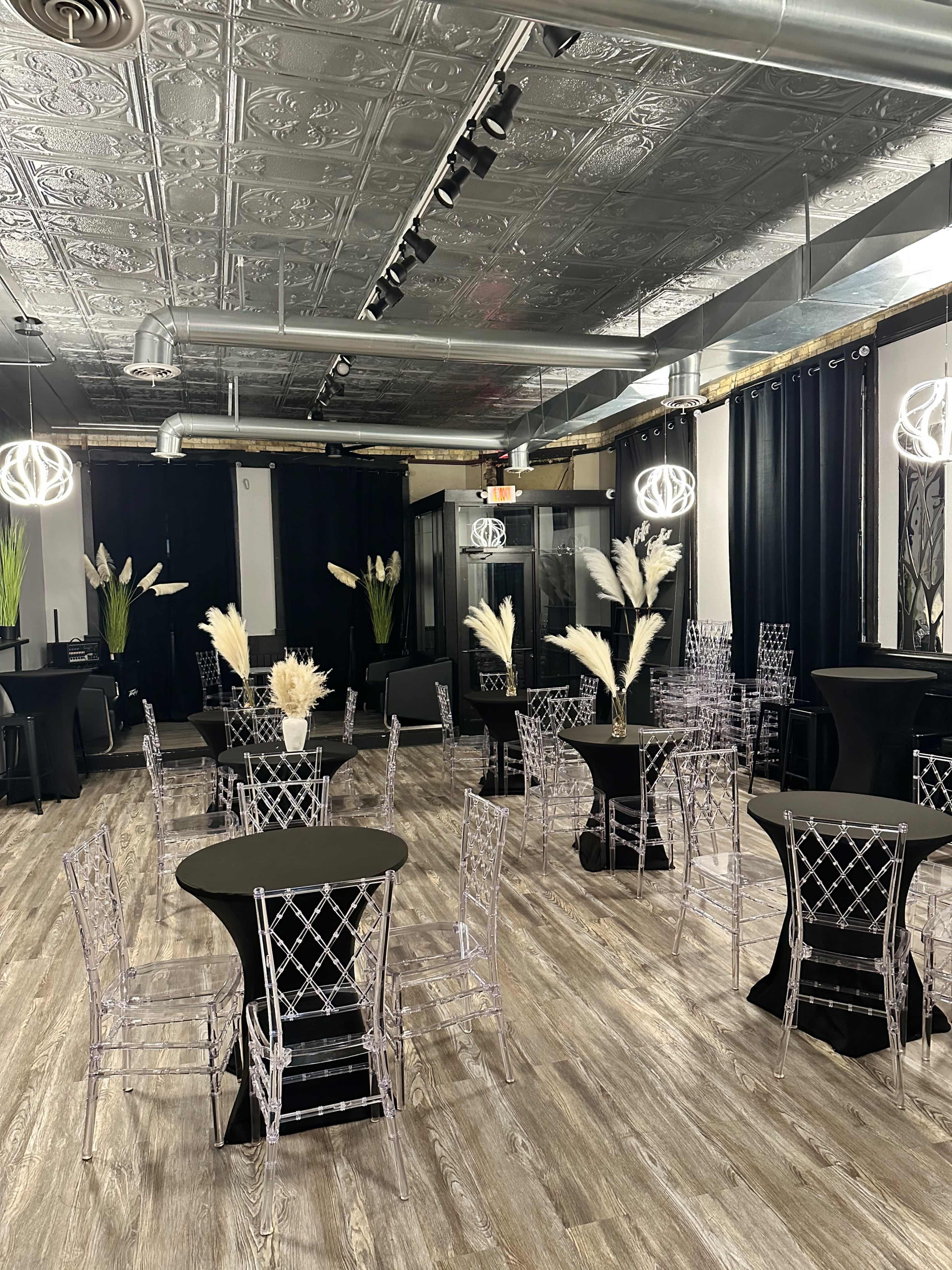 The room features several black tables surrounded by clear acrylic chairs, with decorative plants and modern light fixtures adding to the ambiance.