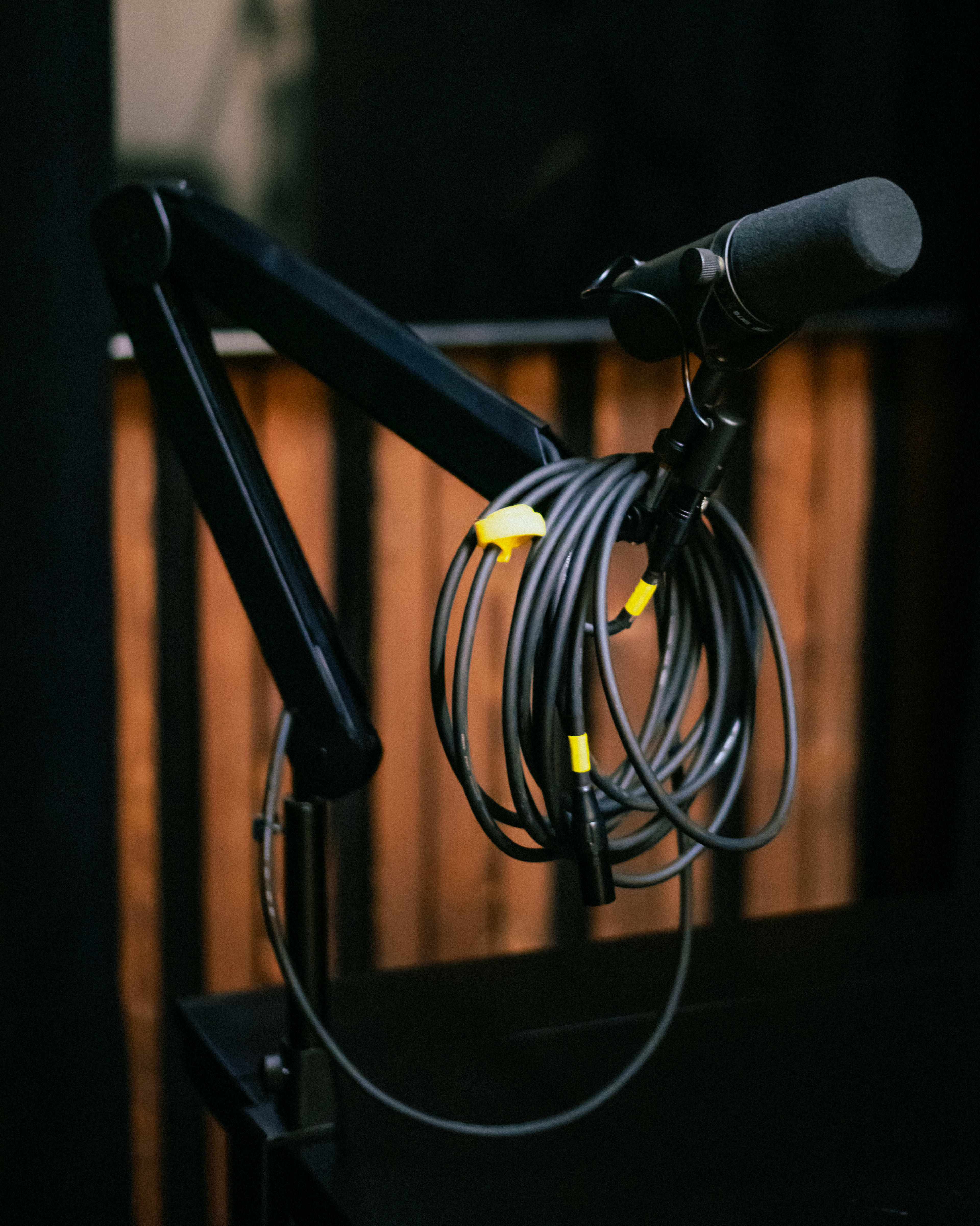 A microphone is suspended from a black arm, with its cables coiled and secured, set against a dark background.