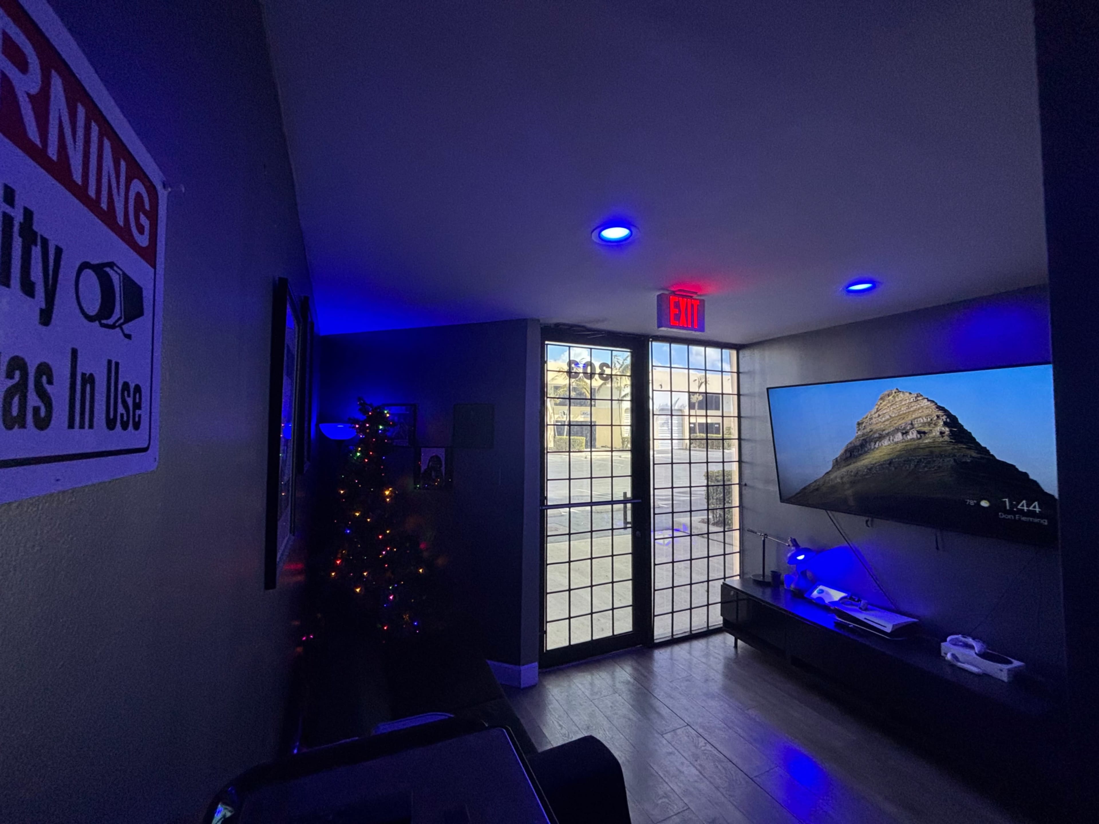 The image shows a room with a flat-screen TV displaying a mountain landscape, dim lighting with blue hues, and a decorative Christmas tree in the corner.