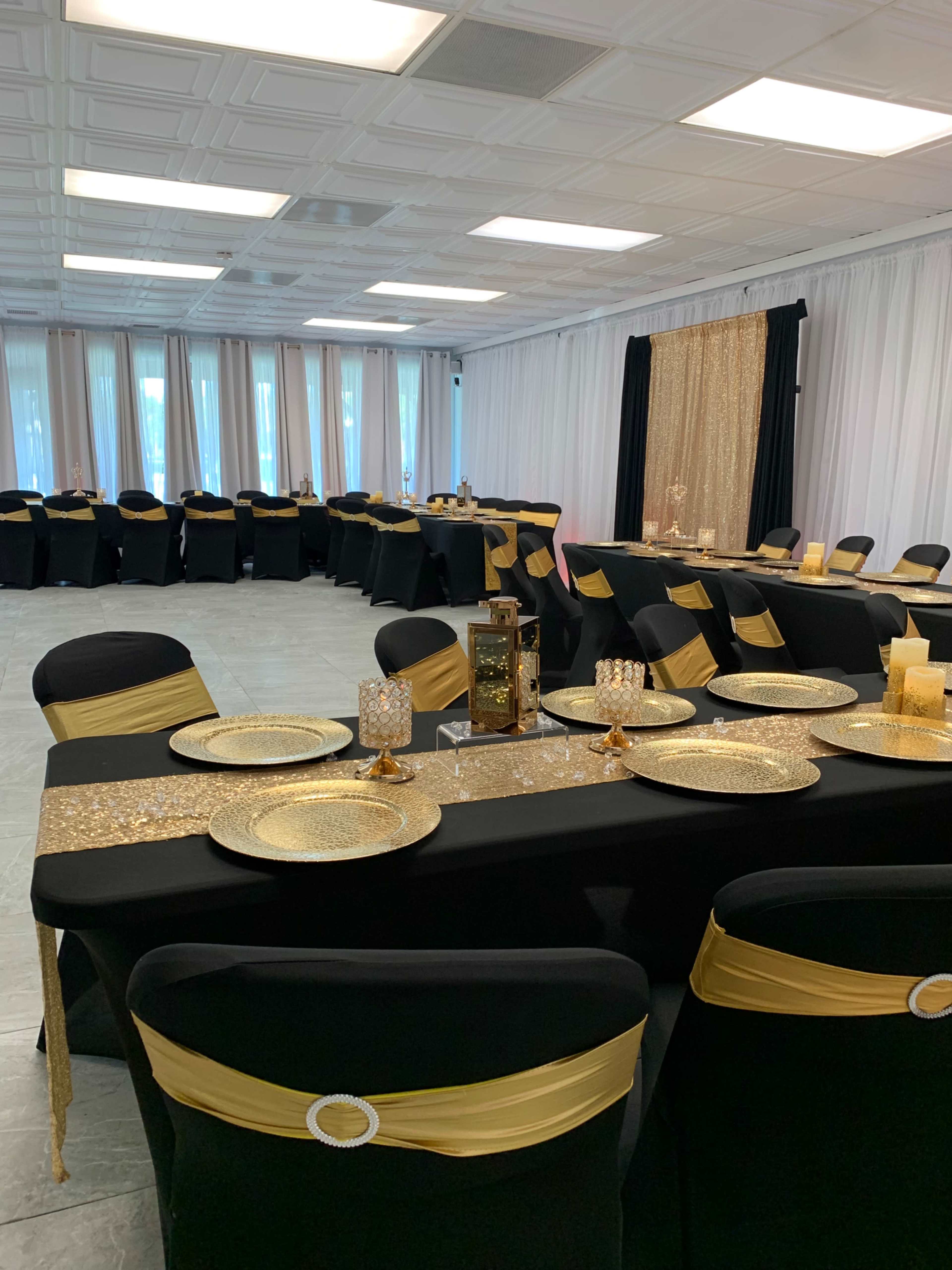 A banquet hall is set up with multiple tables covered in black linens and adorned with gold accents.