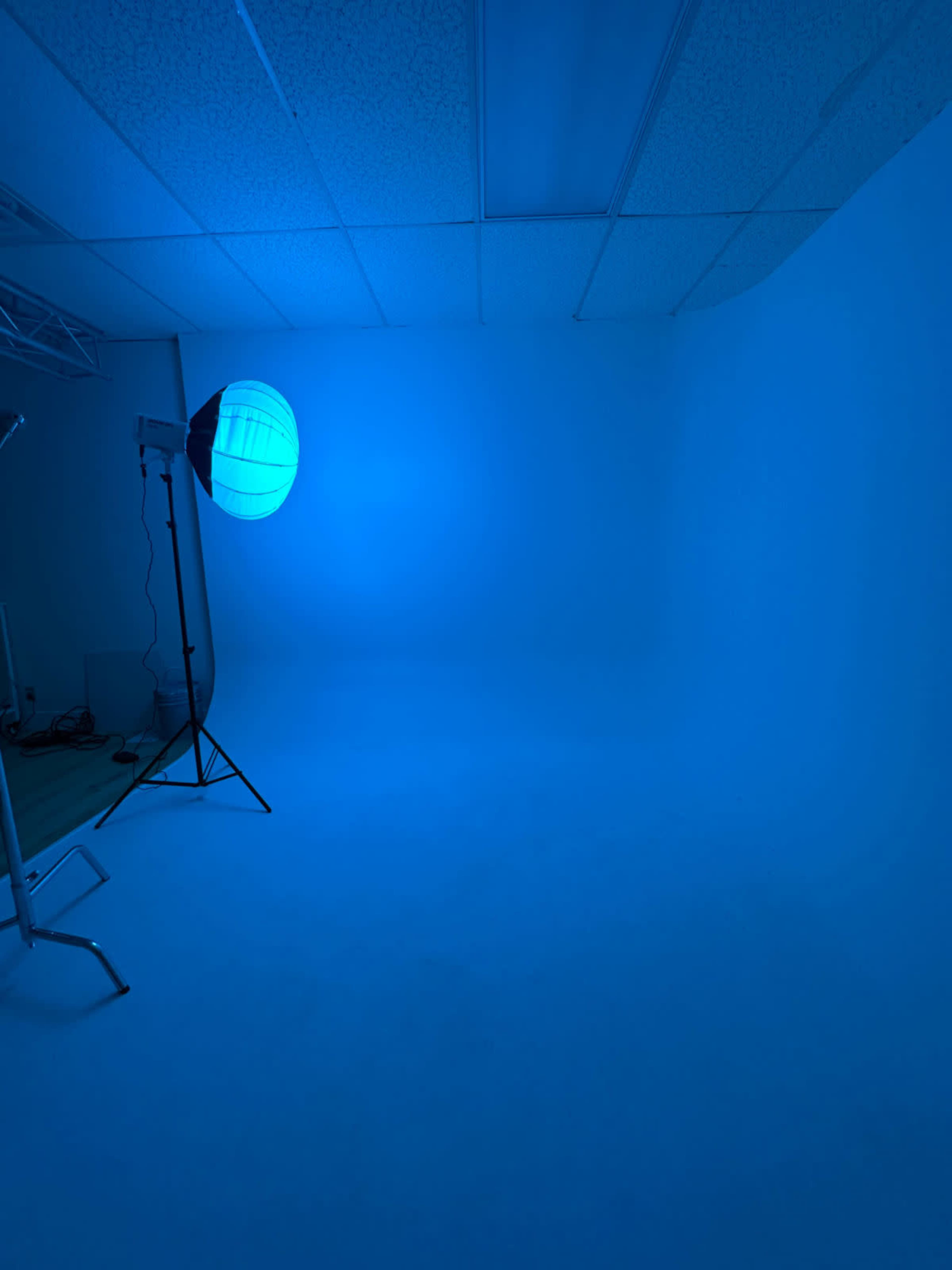 The image shows a photography studio with a blue backdrop and a softbox light positioned on a stand.