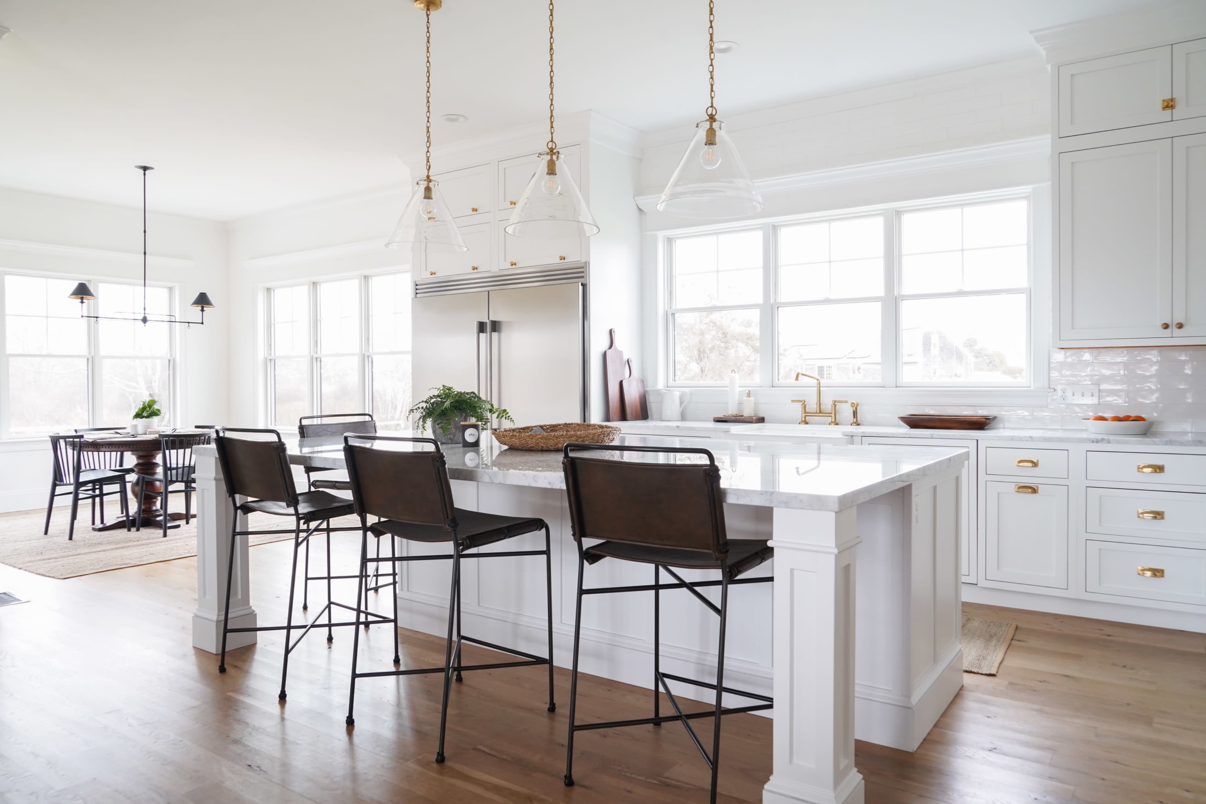 A bright kitchen features a white island with four black bar stools and large windows that provide abundant natural light.
