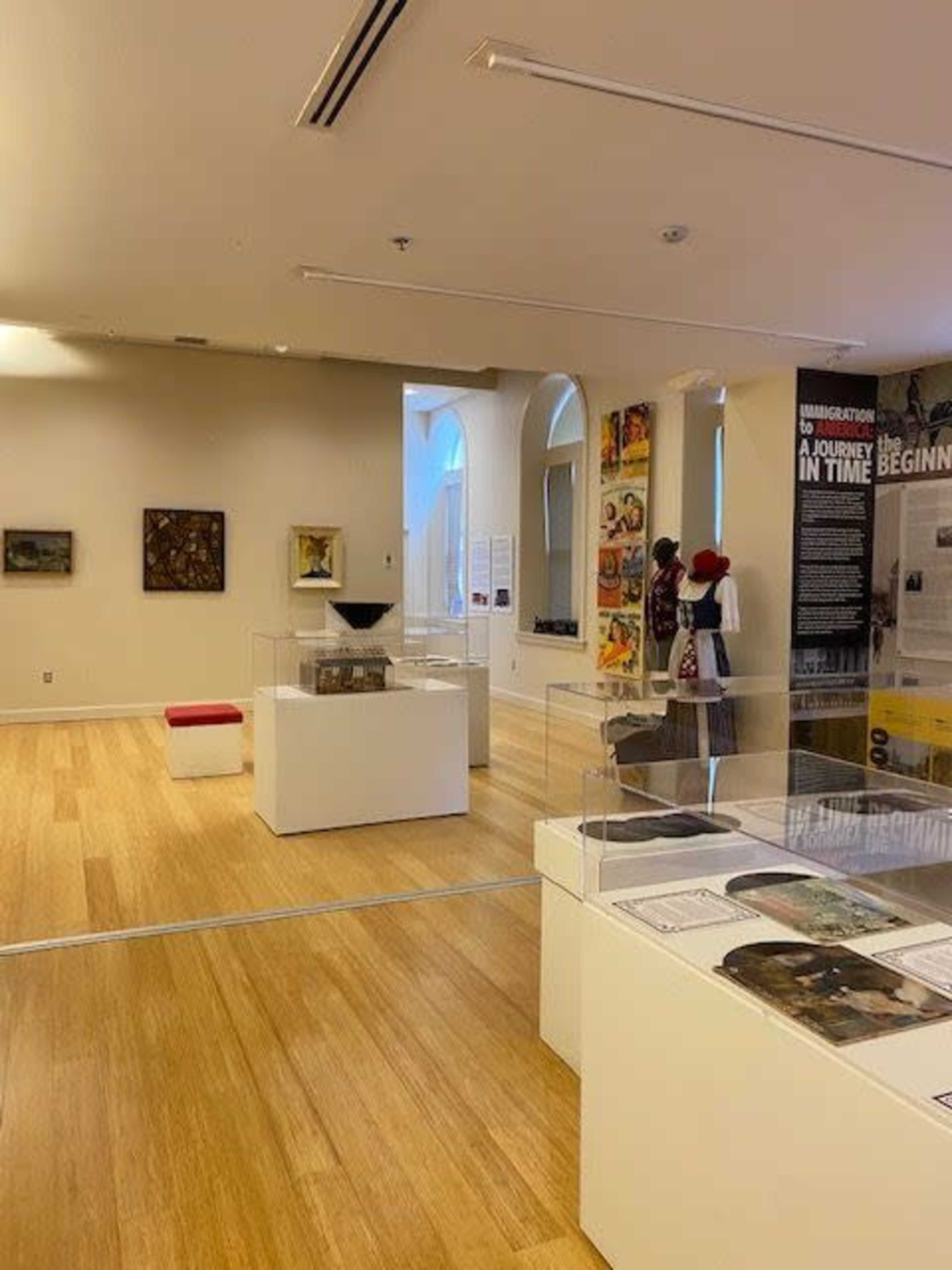 A spacious museum gallery featuring various art pieces and displays, including sculptures, paintings, and informational panels.