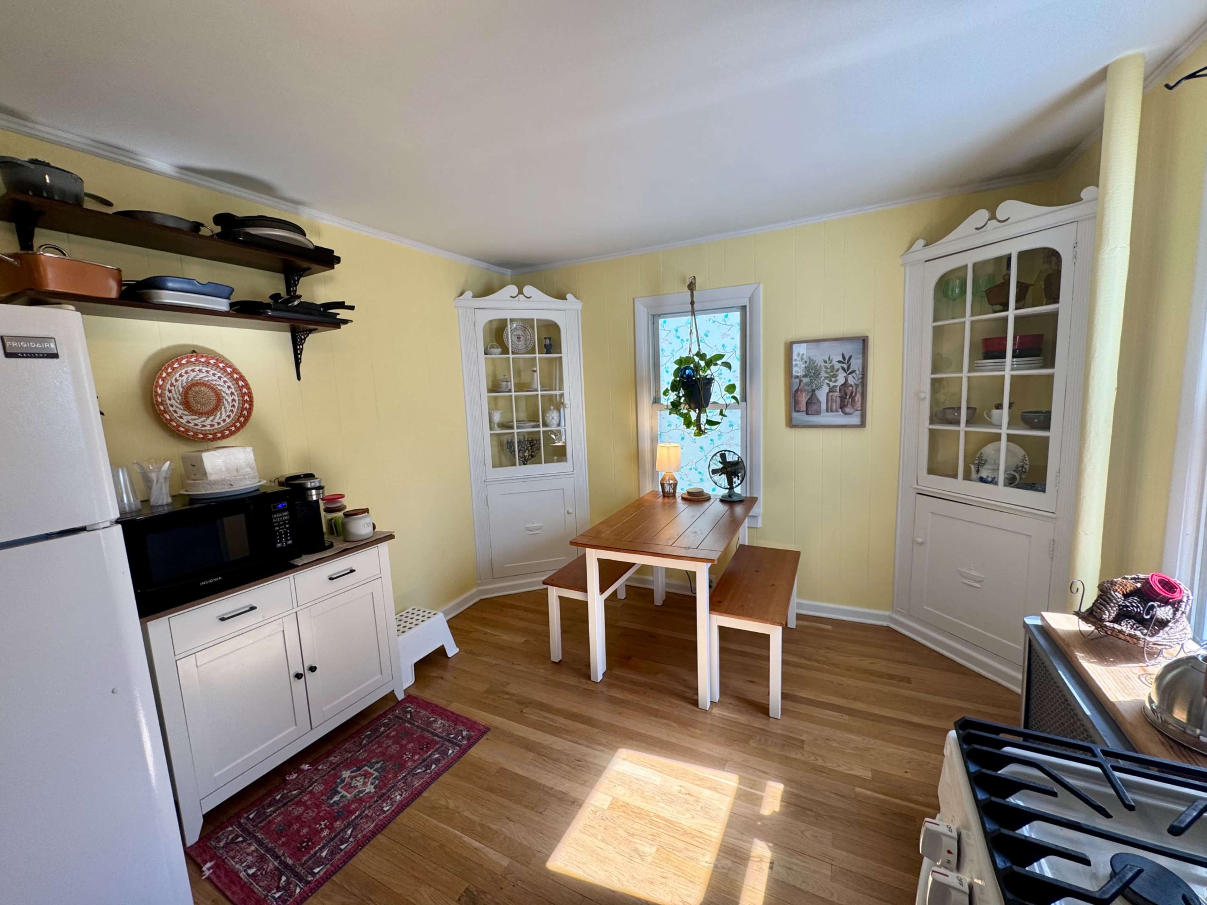 The kitchen features white cabinetry, a wooden table, and natural light streaming through a window.