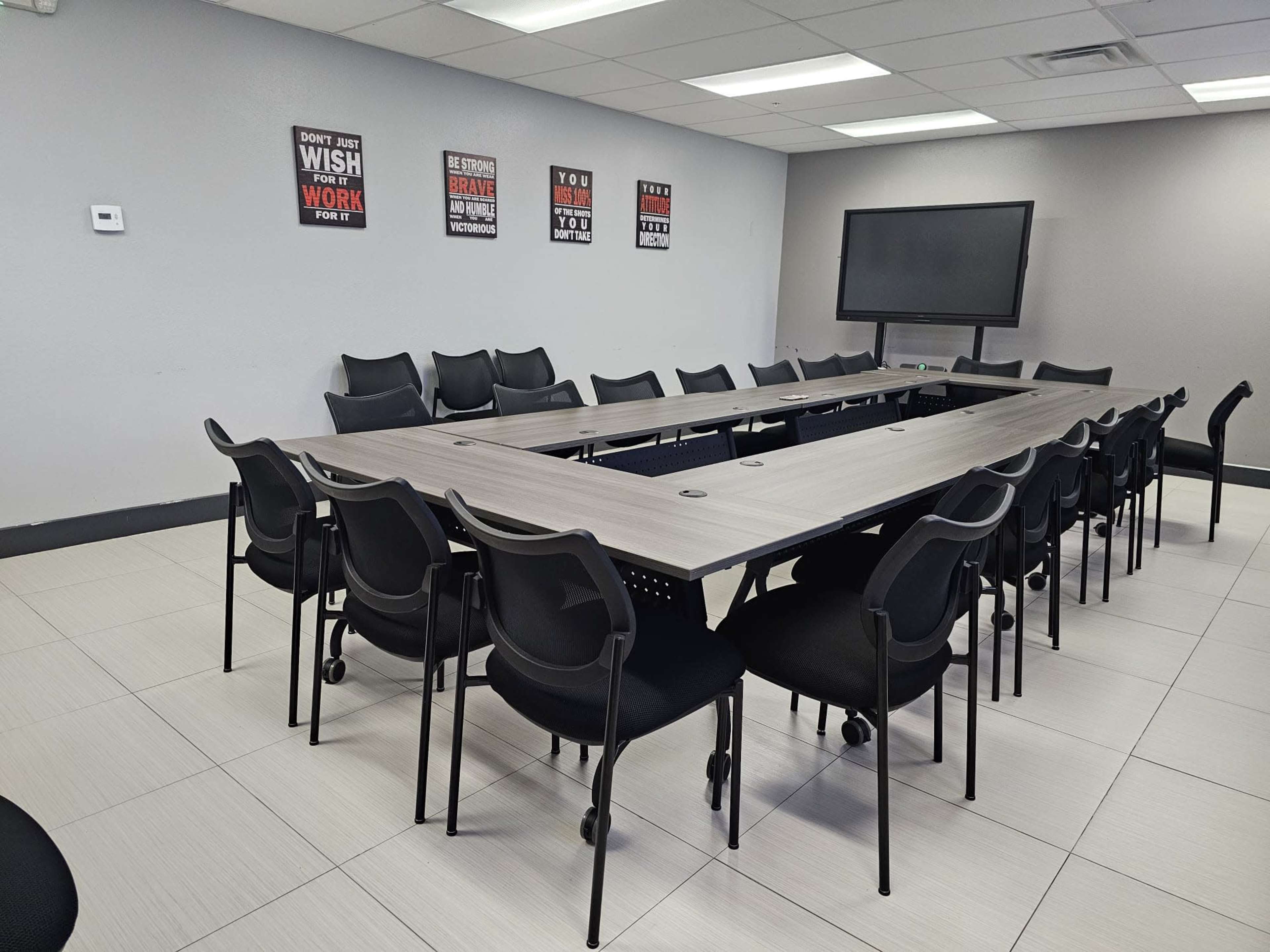 A large conference room features a long rectangular table surrounded by black rolling chairs and motivational posters on the walls.