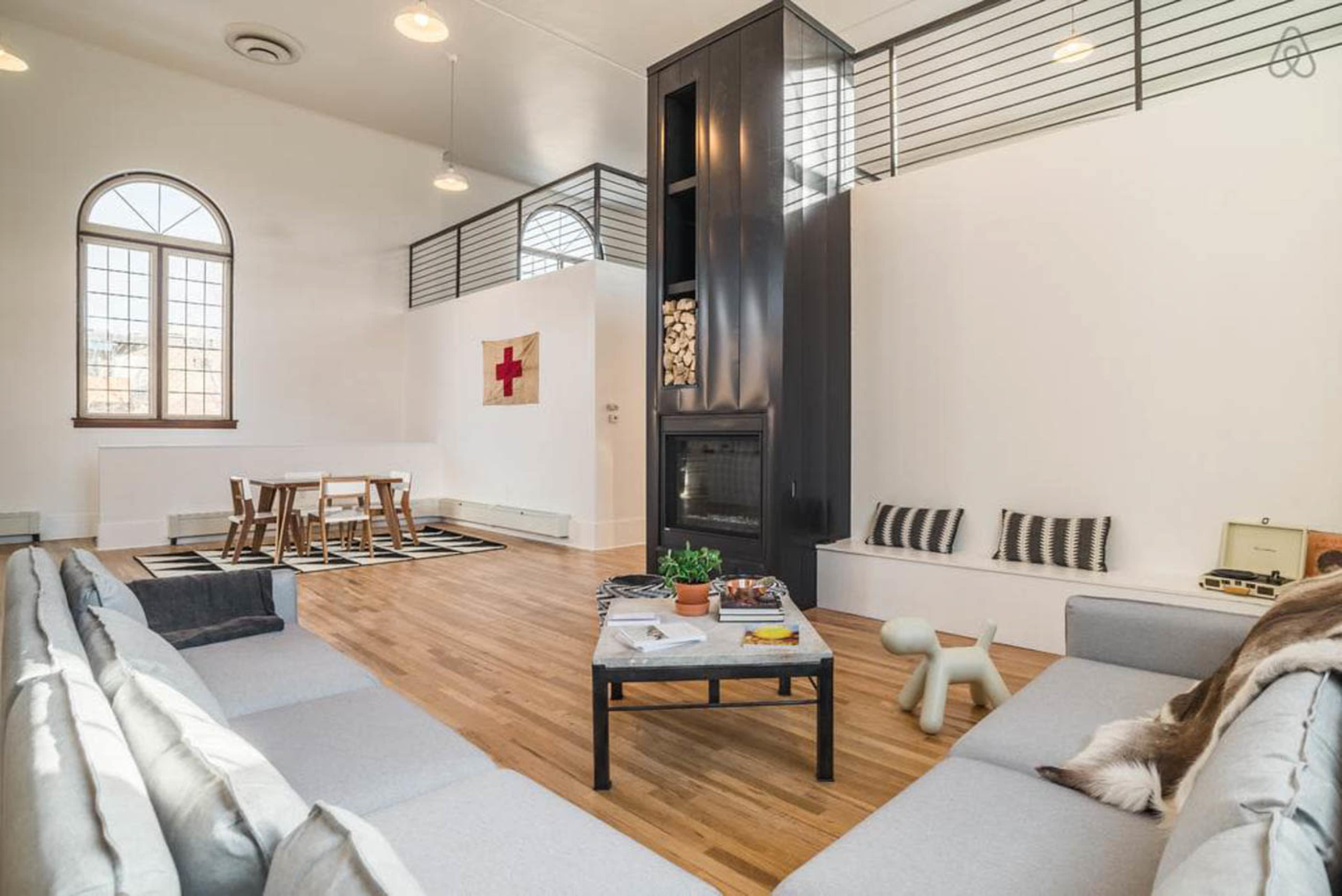 A spacious living room with modern furnishings, including a gray sectional sofa, a wooden dining table, and a central fireplace.