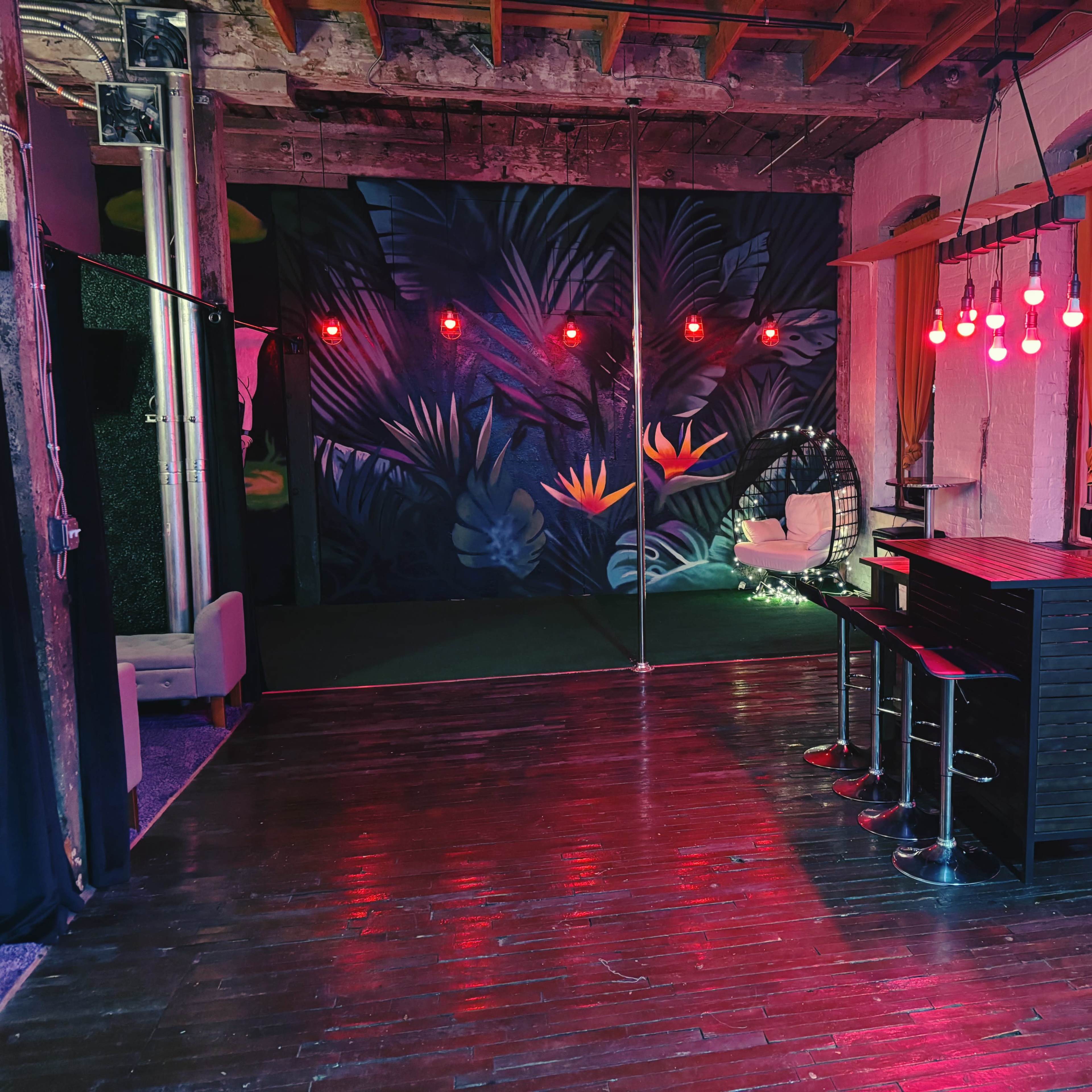 An interior space with a dark floral mural, a seating area, a pole, and red pendant lights.
