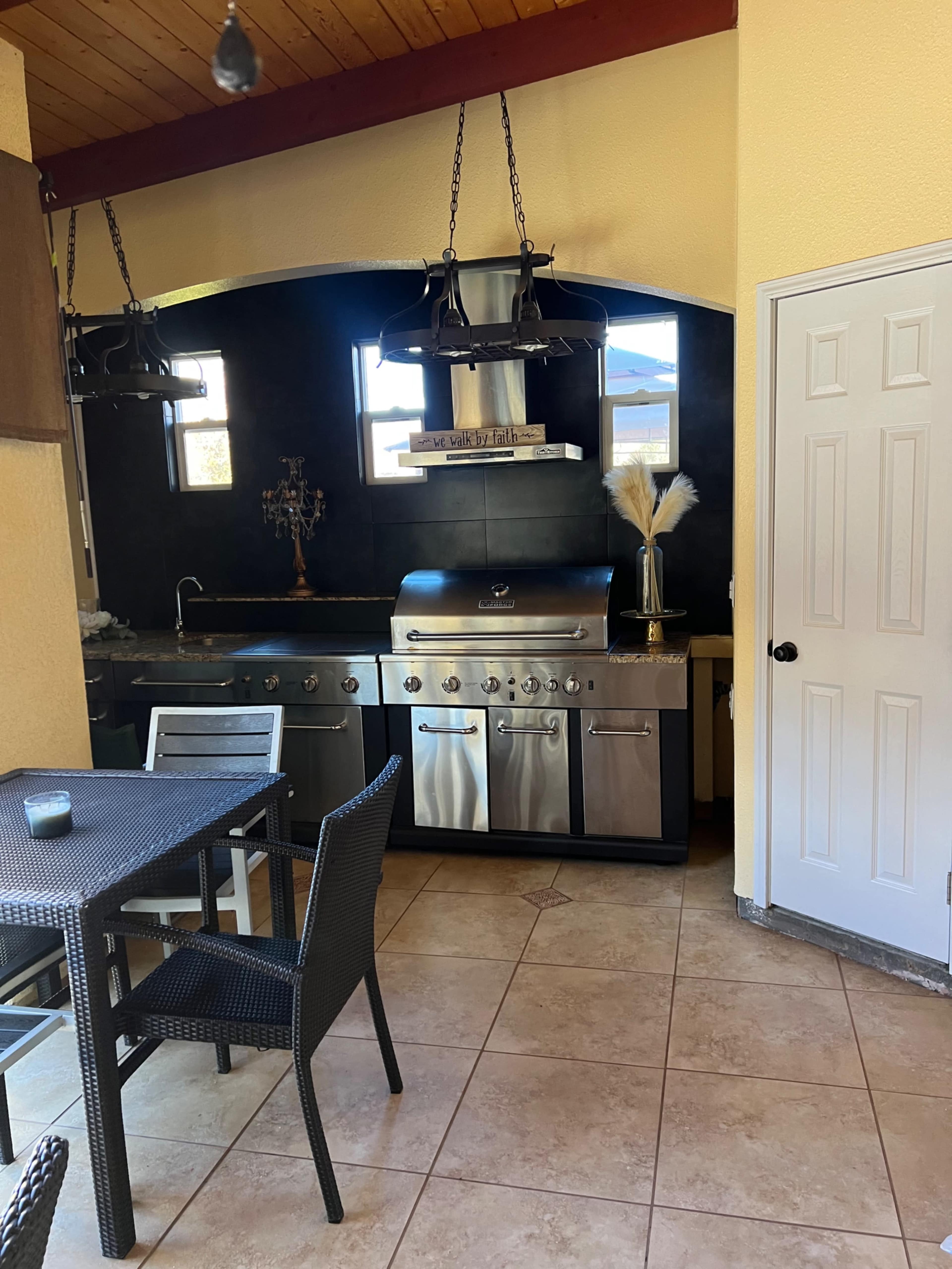 An outdoor kitchen area featuring a stainless steel barbecue grill, a countertop, and a dining table with chairs.