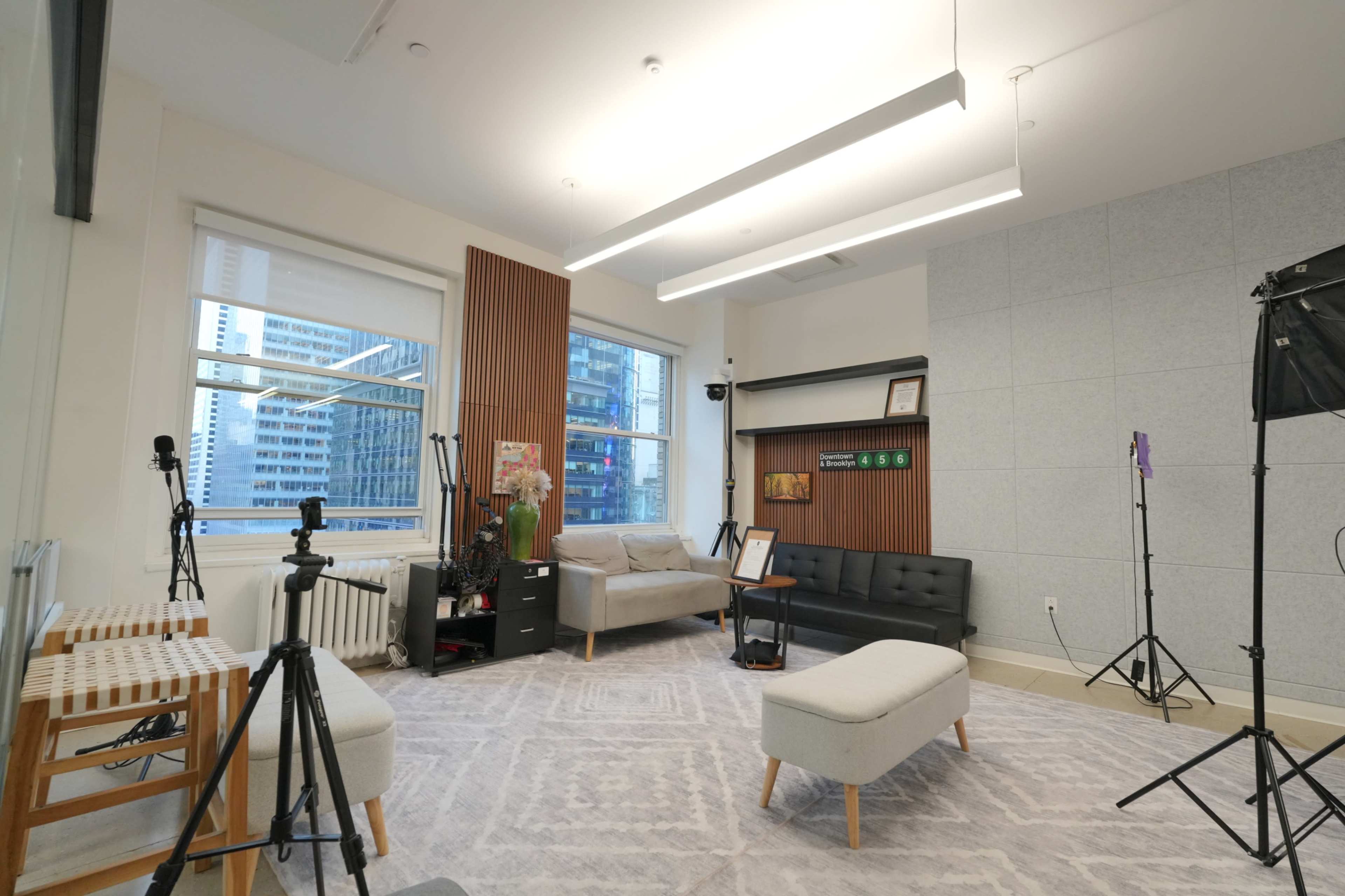 The image shows a modern room with a gray carpet, various seating areas, and equipment for video recording.