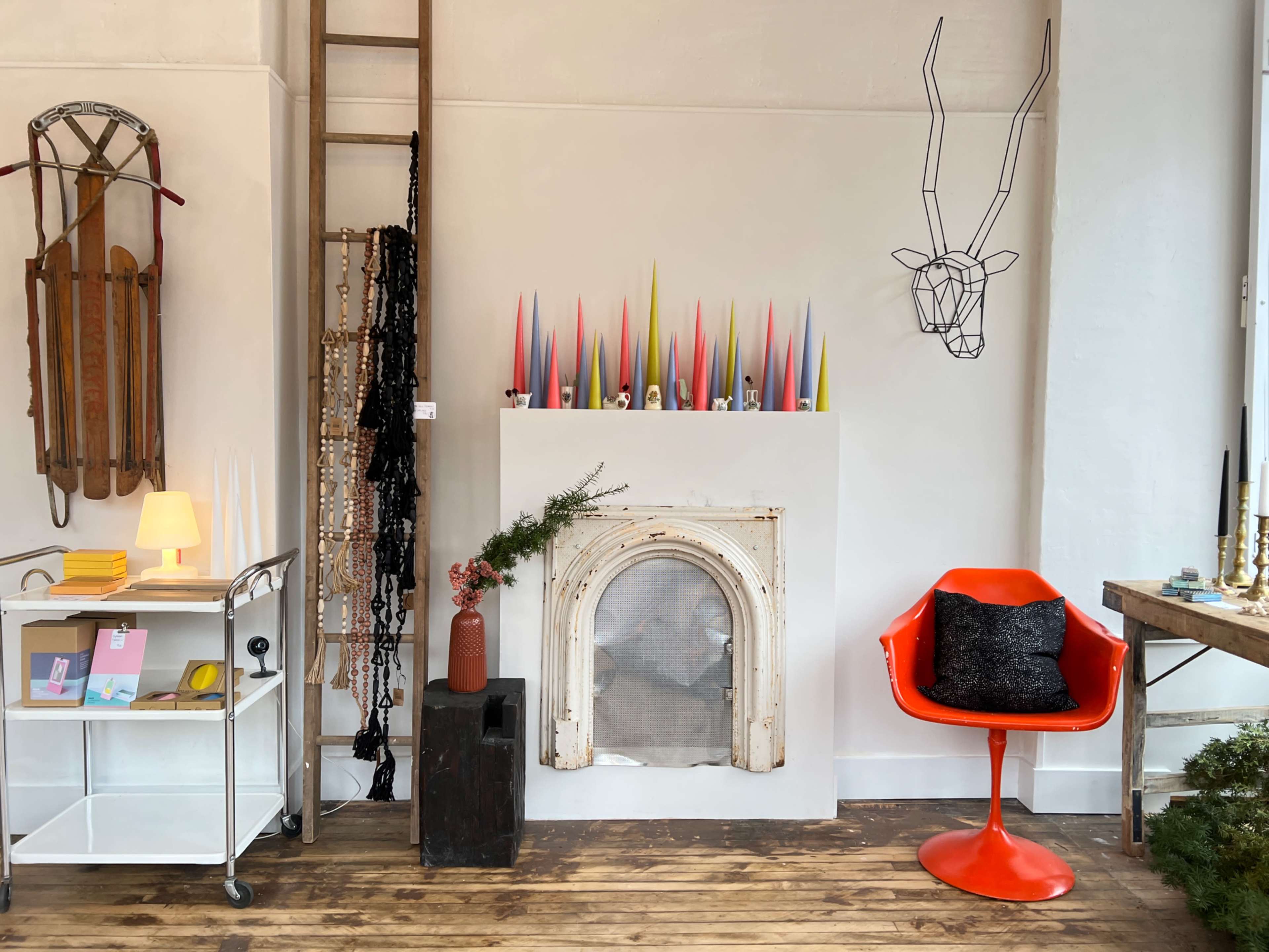 A cozy interior featuring a white wall with colorful candles above a decorative fireplace, an orange chair, and various decorative items scattered around.