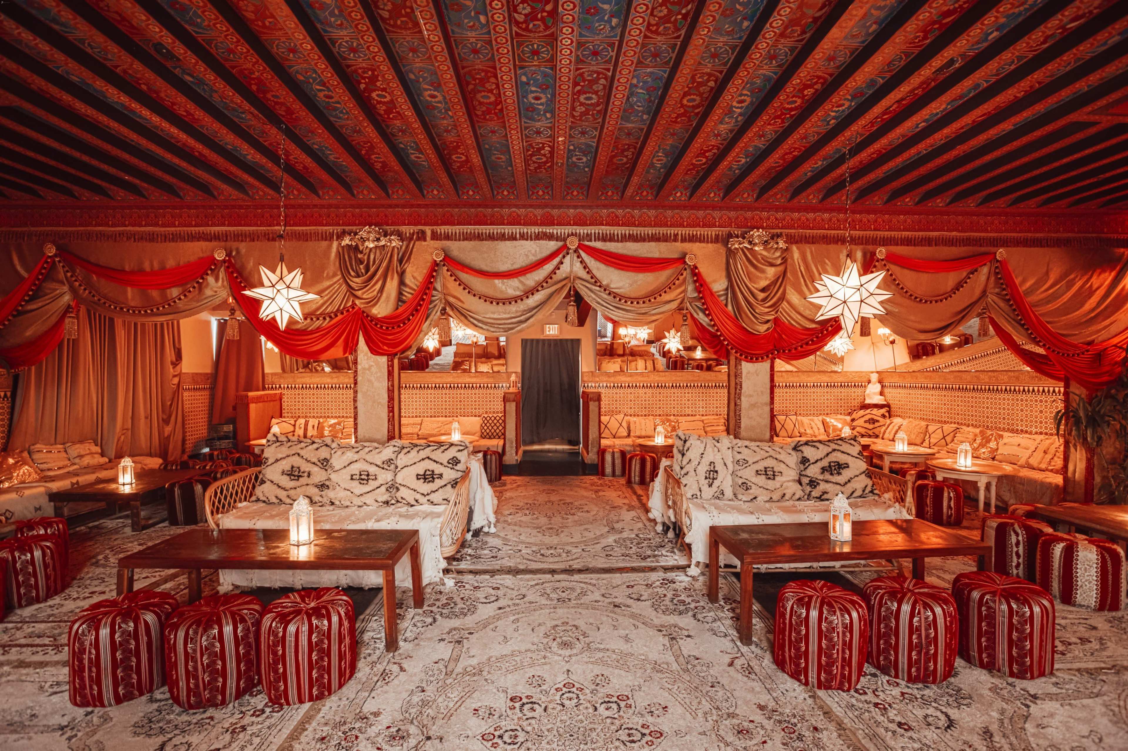 A lavishly decorated interior with intricately patterned ceilings, patterned carpets, plush seating areas, and lanterns illuminating the space.
