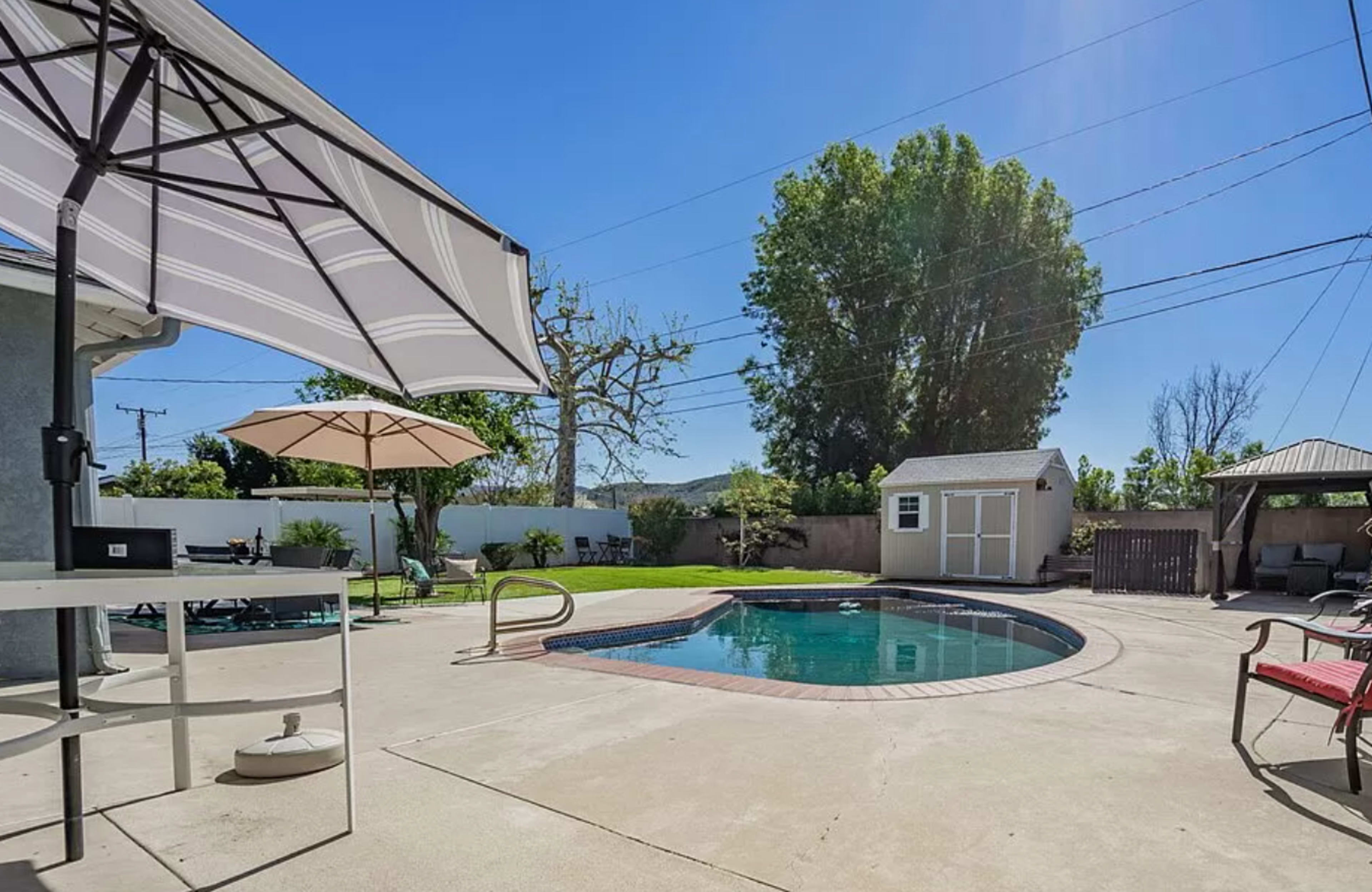 A backyard with a swimming pool surrounded by patio furniture, an umbrella, and a small storage shed nearby.