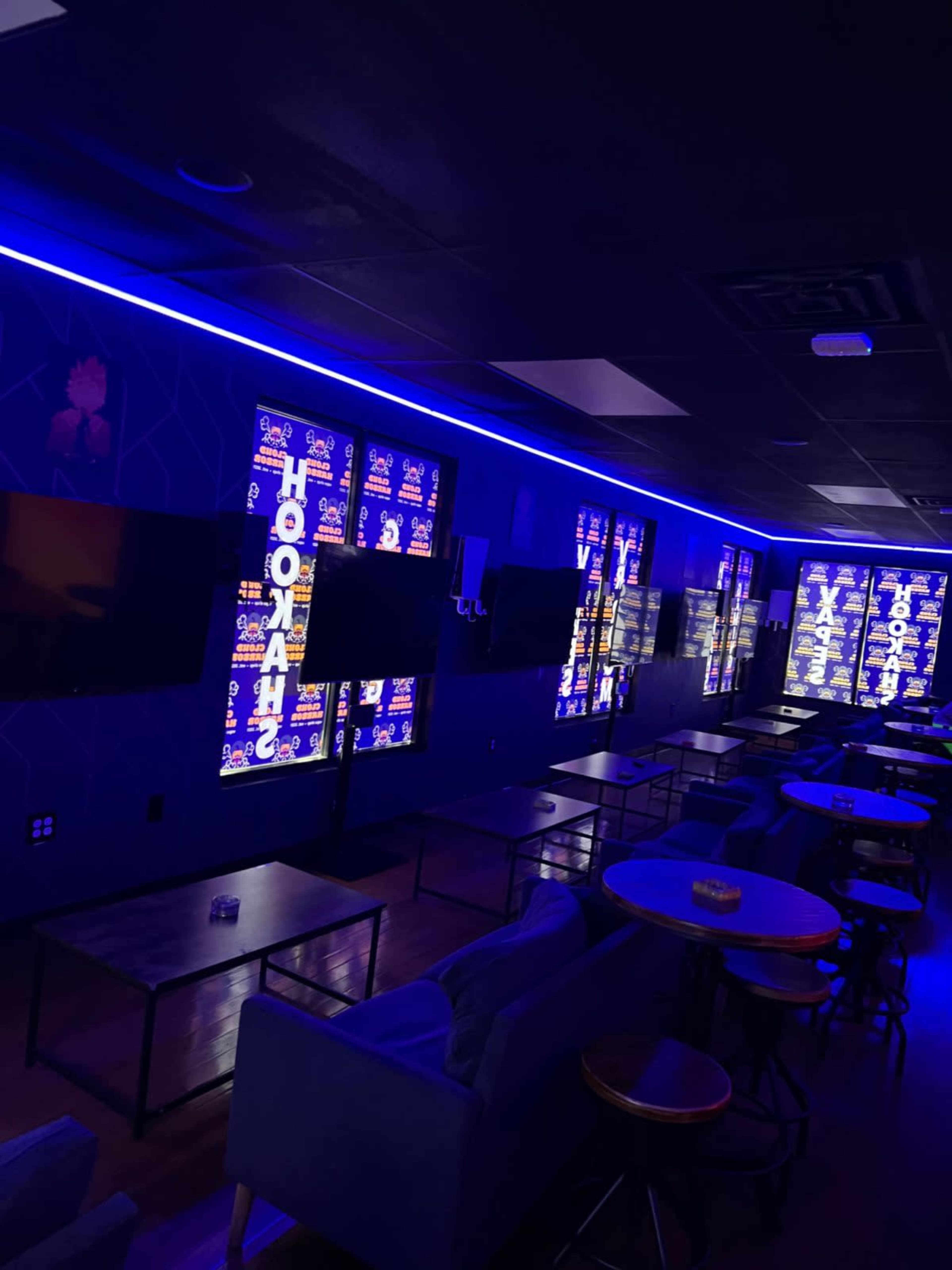 The image shows an interior of a lounge featuring dark blue walls, illuminated signage, and several seating areas with tables.