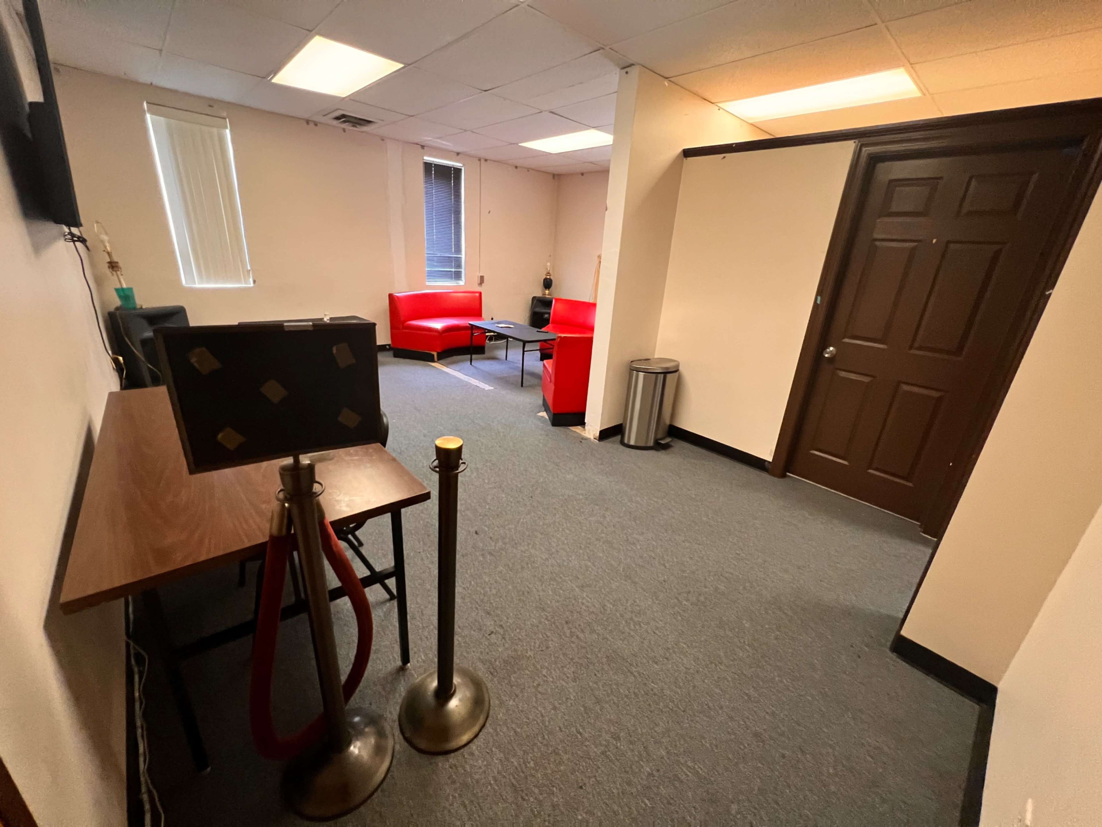 A room with a blue carpet, two red chairs, a wooden table, and a closed door on one side.