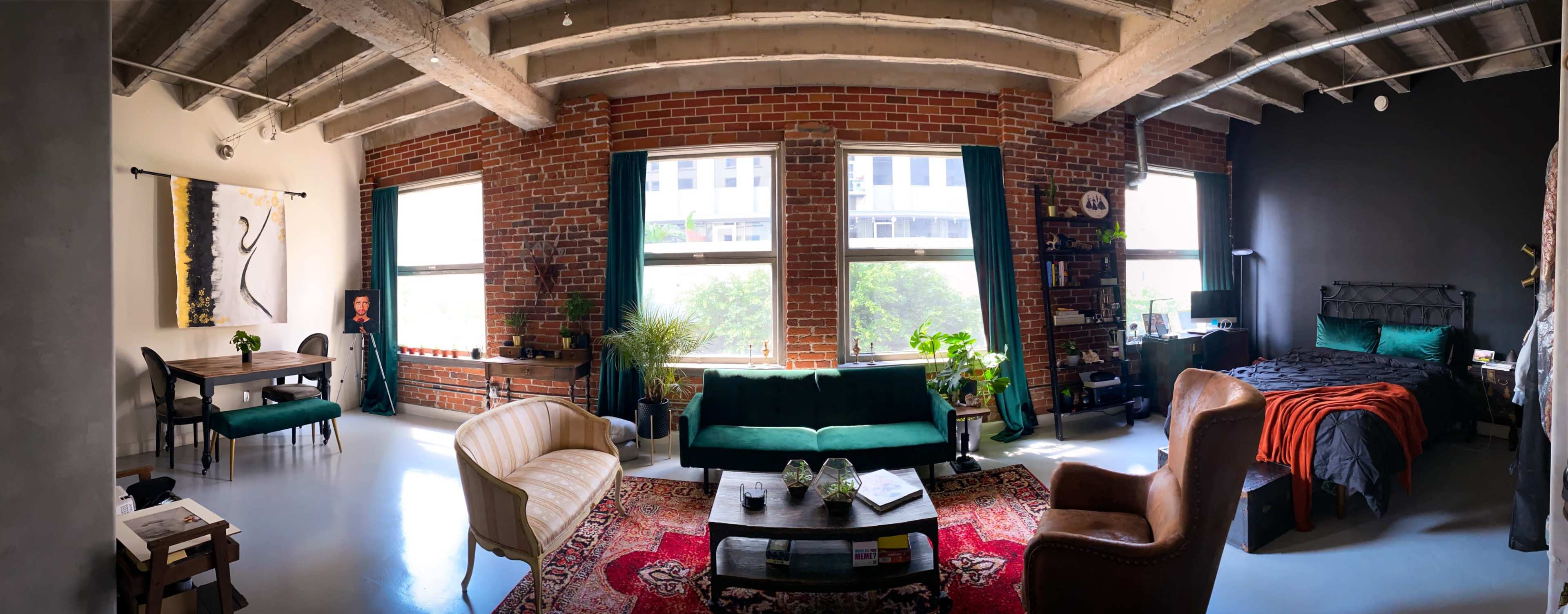 The image depicts a well-decorated loft apartment featuring exposed brick walls, large windows, and a mix of modern and vintage furniture.