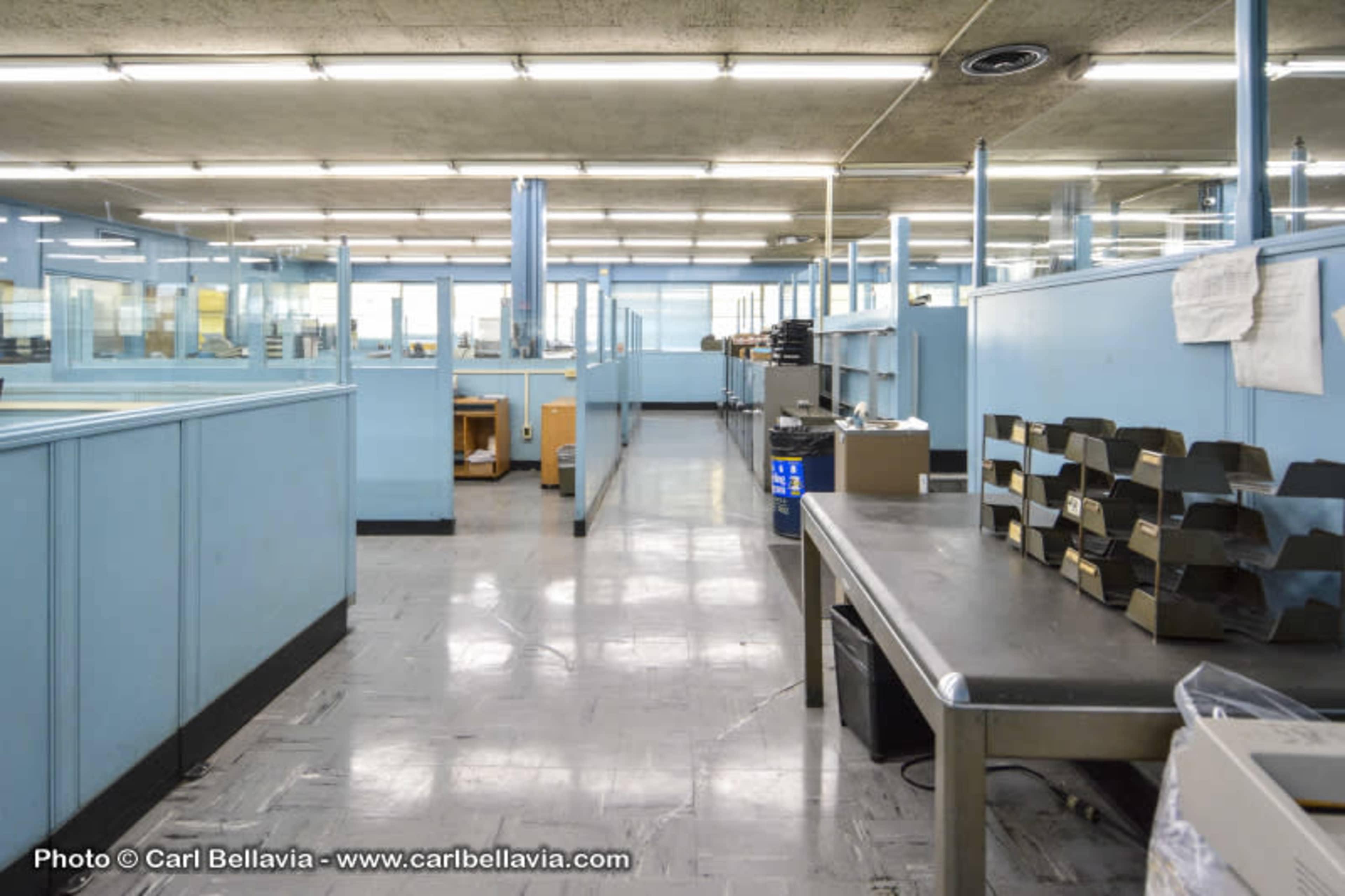 A spacious, empty office area with blue walls, tables, and shelves organized along the sides.
