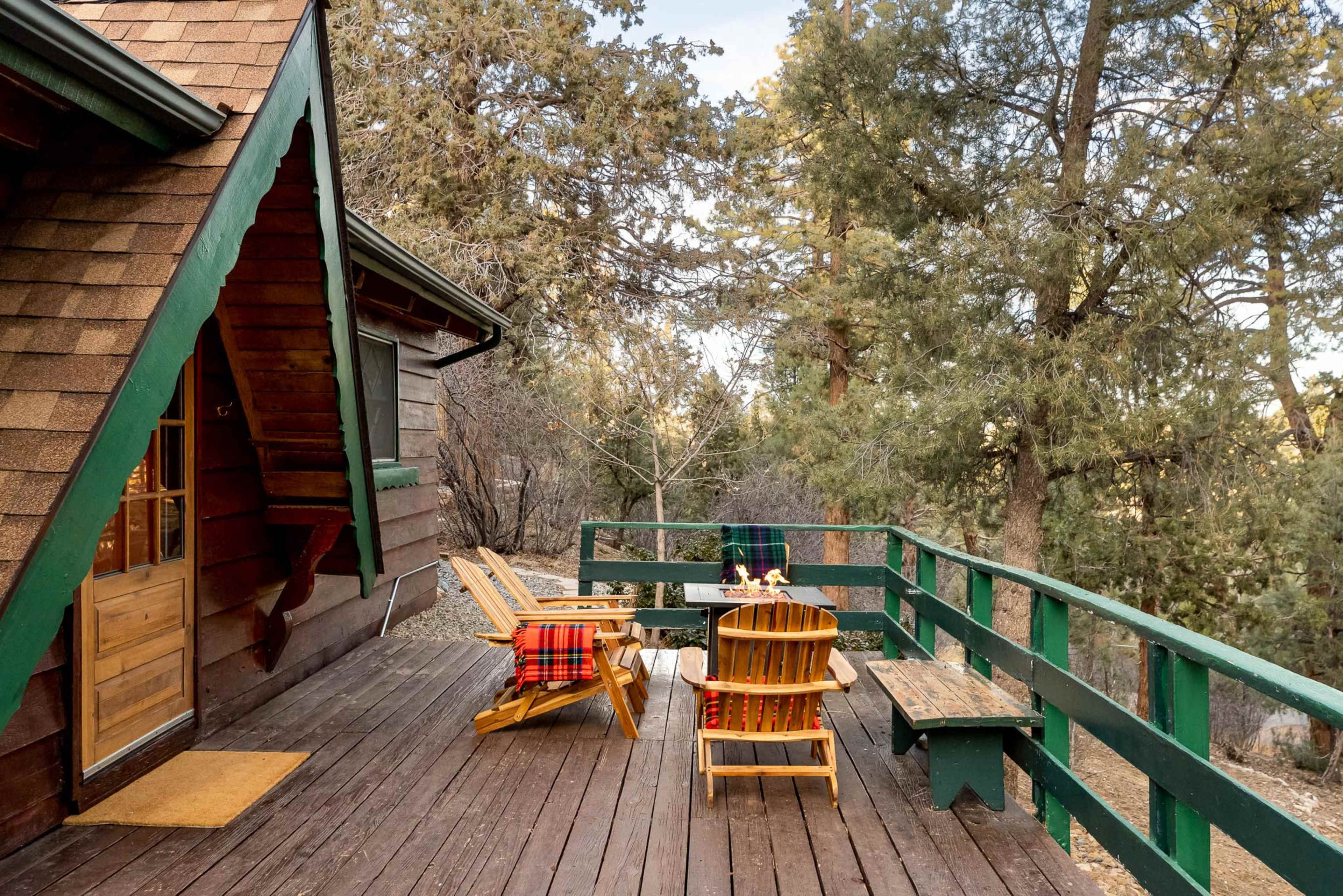 A wooden deck with two Adirondack chairs and a picnic table overlooks a wooded area.