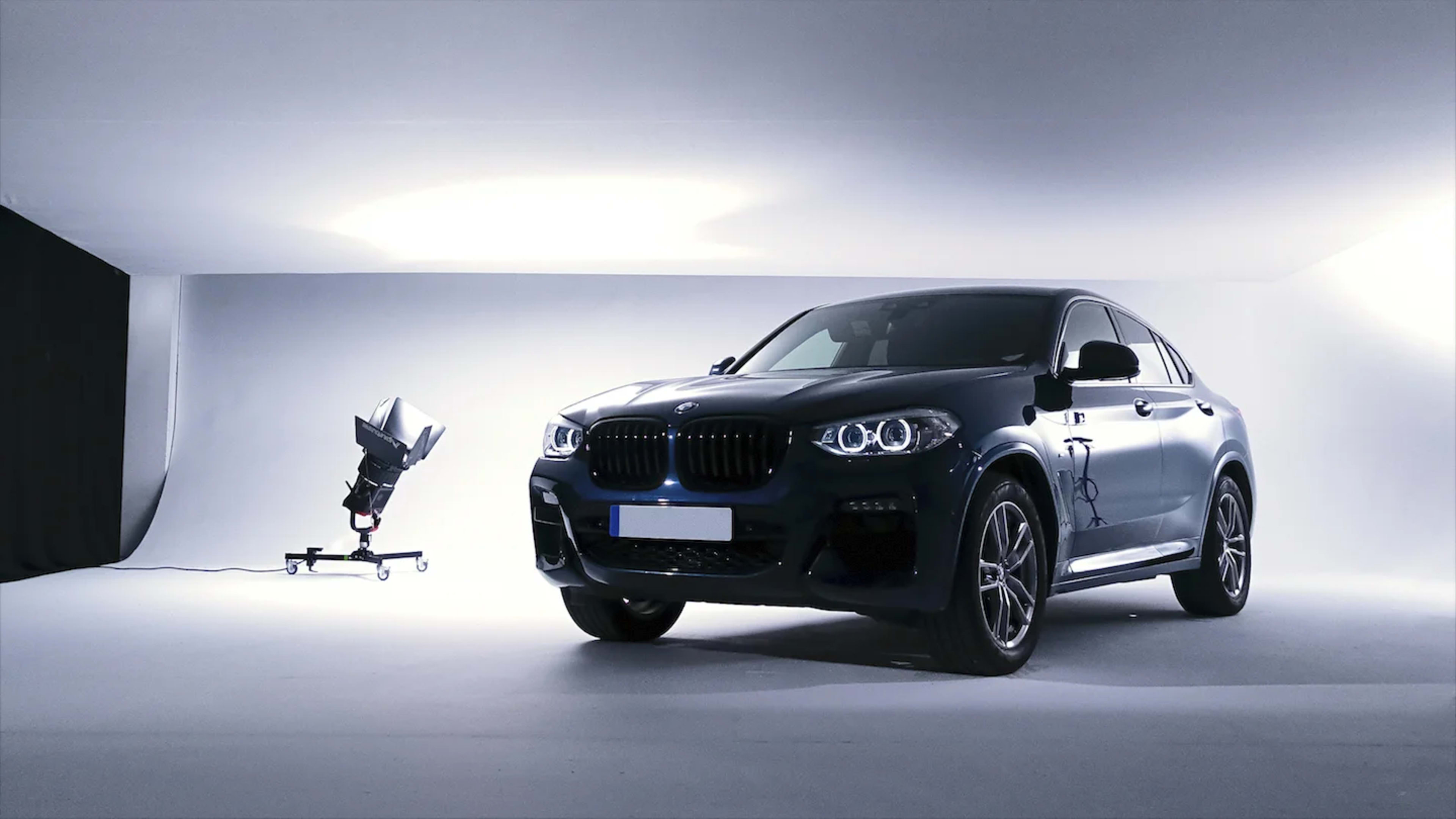 A dark blue BMW X4 is displayed in a studio setting with a spotlight and a light diffuser in the background.