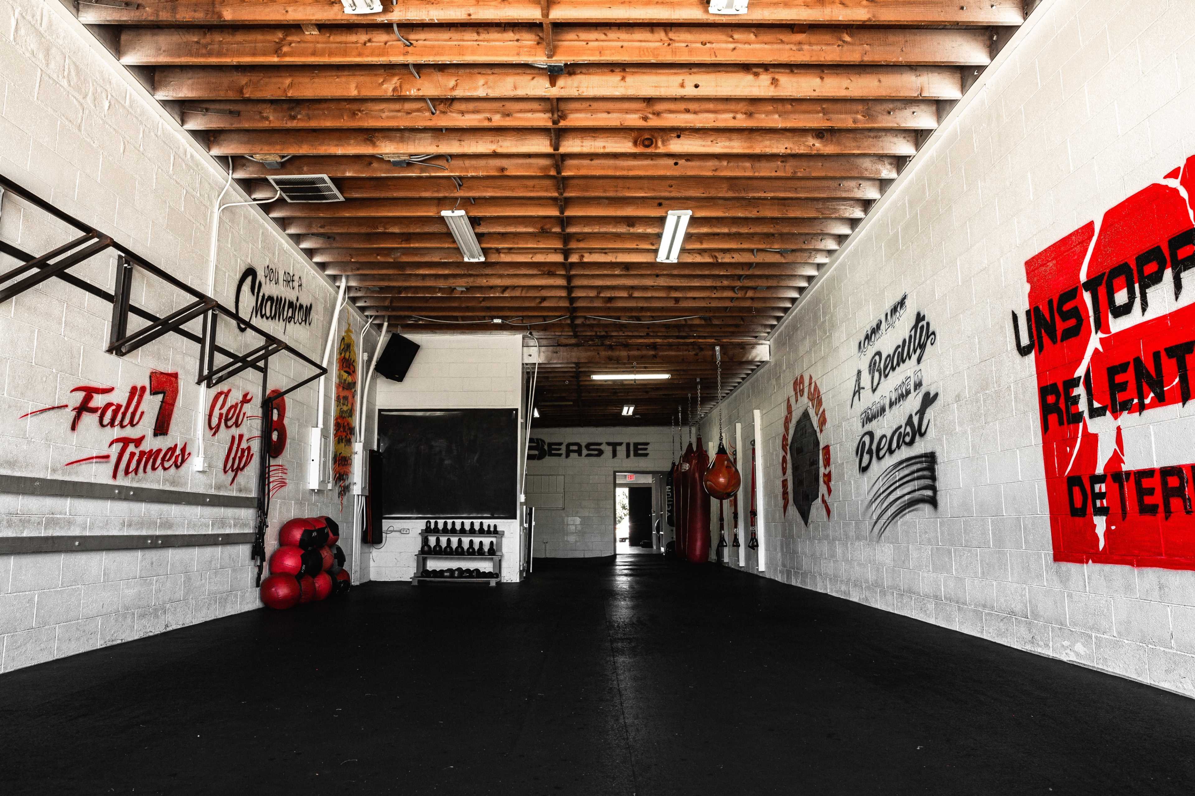 A spacious gym interior with wooden beams, motivational wall art, and exercise equipment along the walls.