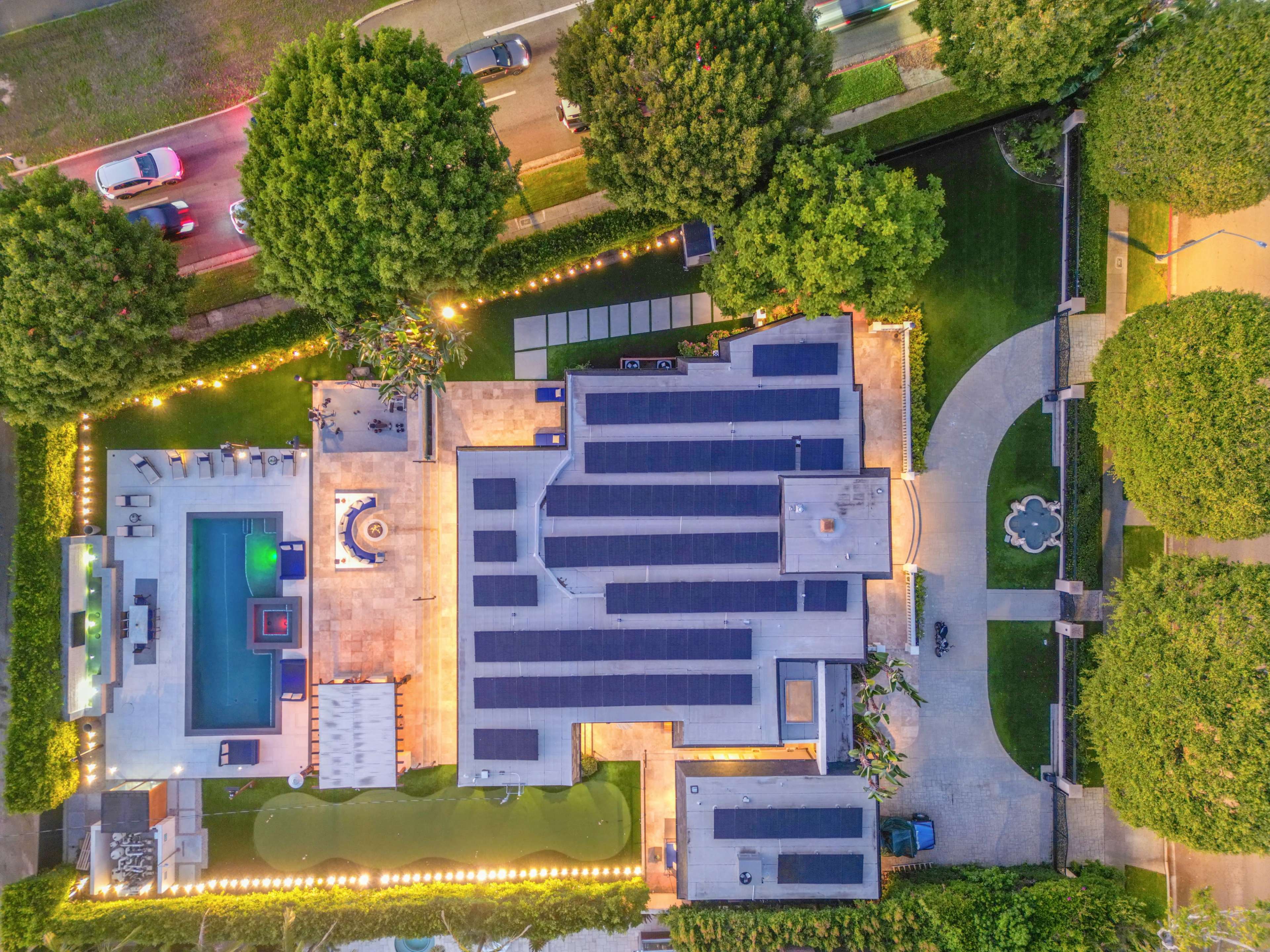 The image shows a large, modern house with a swimming pool, landscaped gardens, and solar panels on the roof, viewed from above.