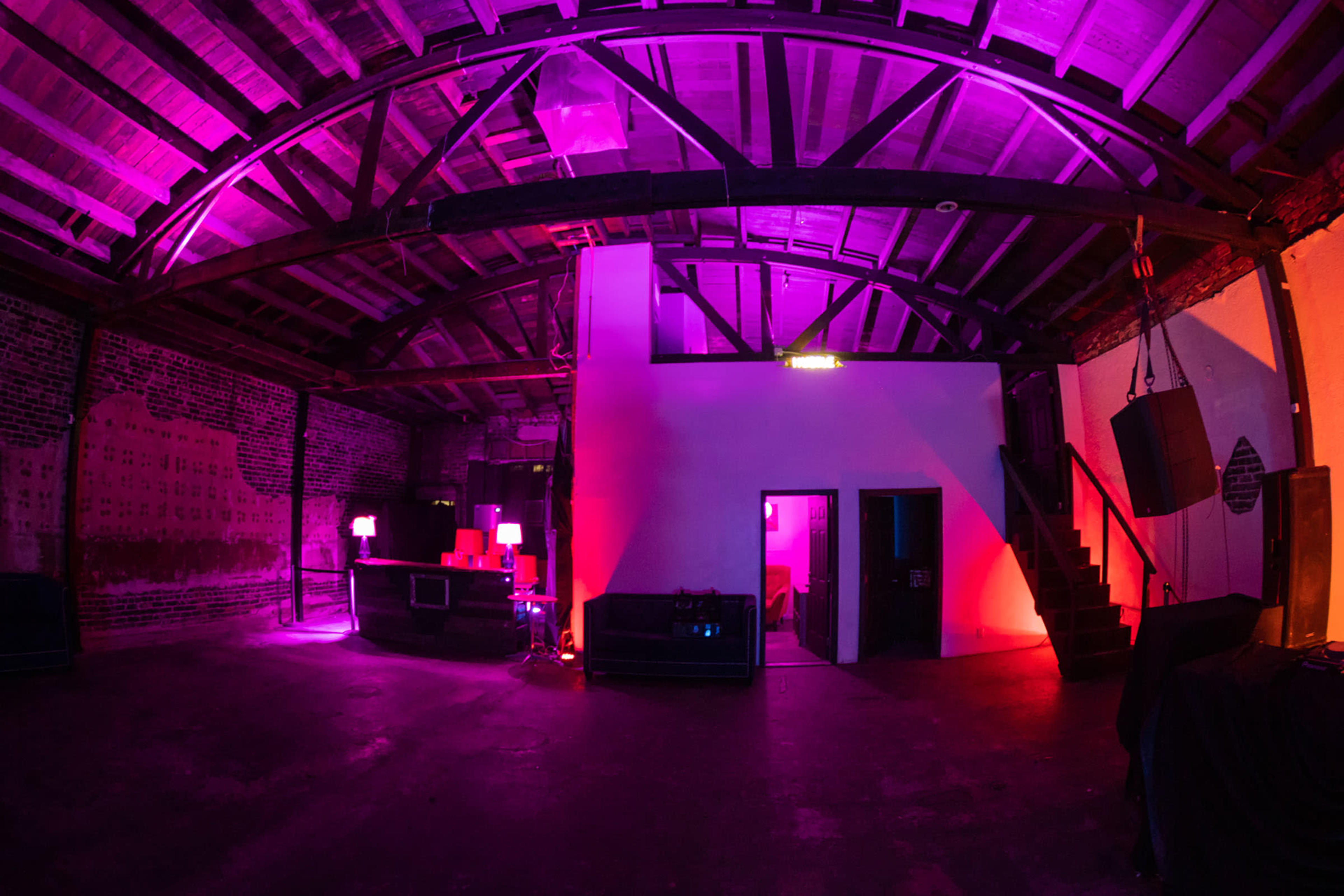 The image shows an industrial-style room with exposed brick walls and wooden beams, illuminated by purple and pink lighting.