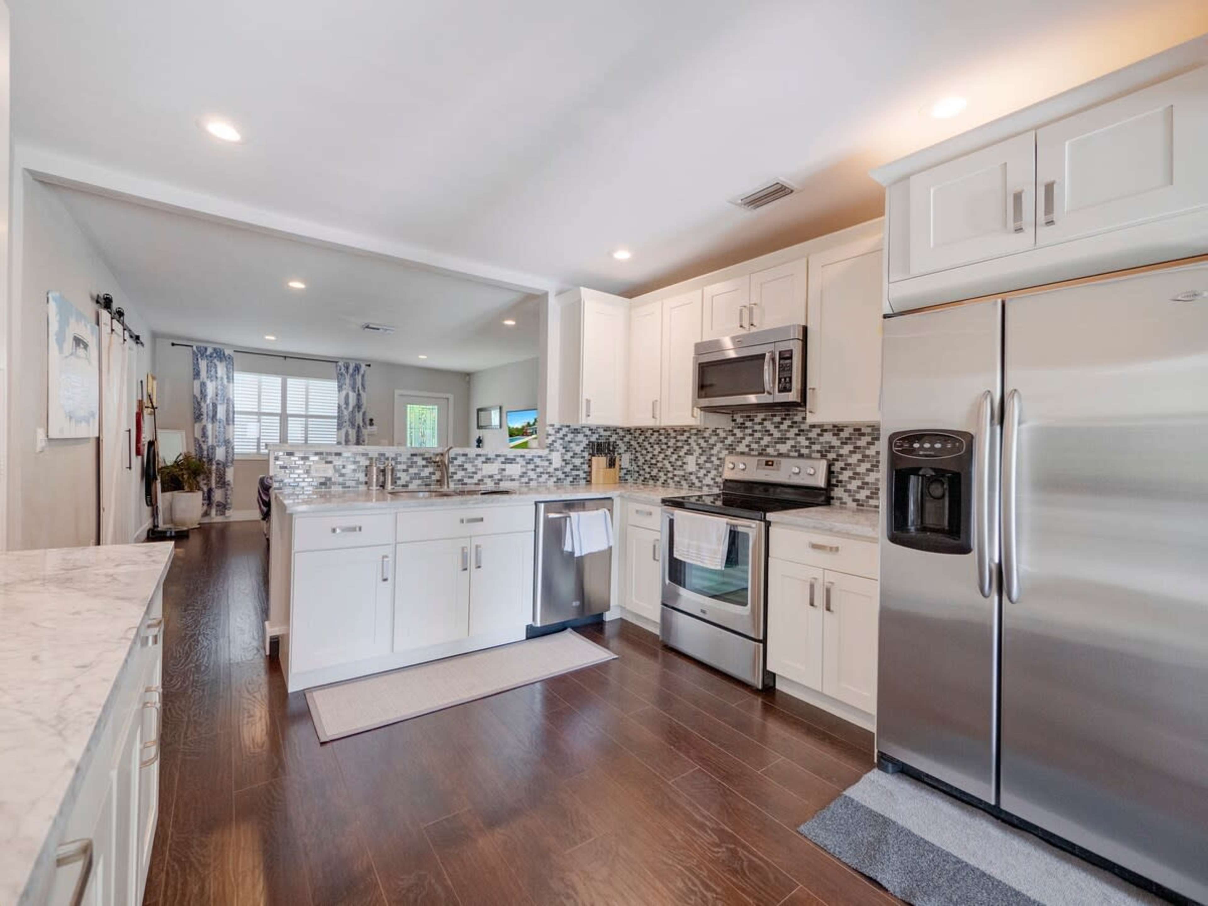 A modern kitchen with white cabinets, stainless steel appliances, and a tiled backsplash, featuring a view into an adjoining living space.