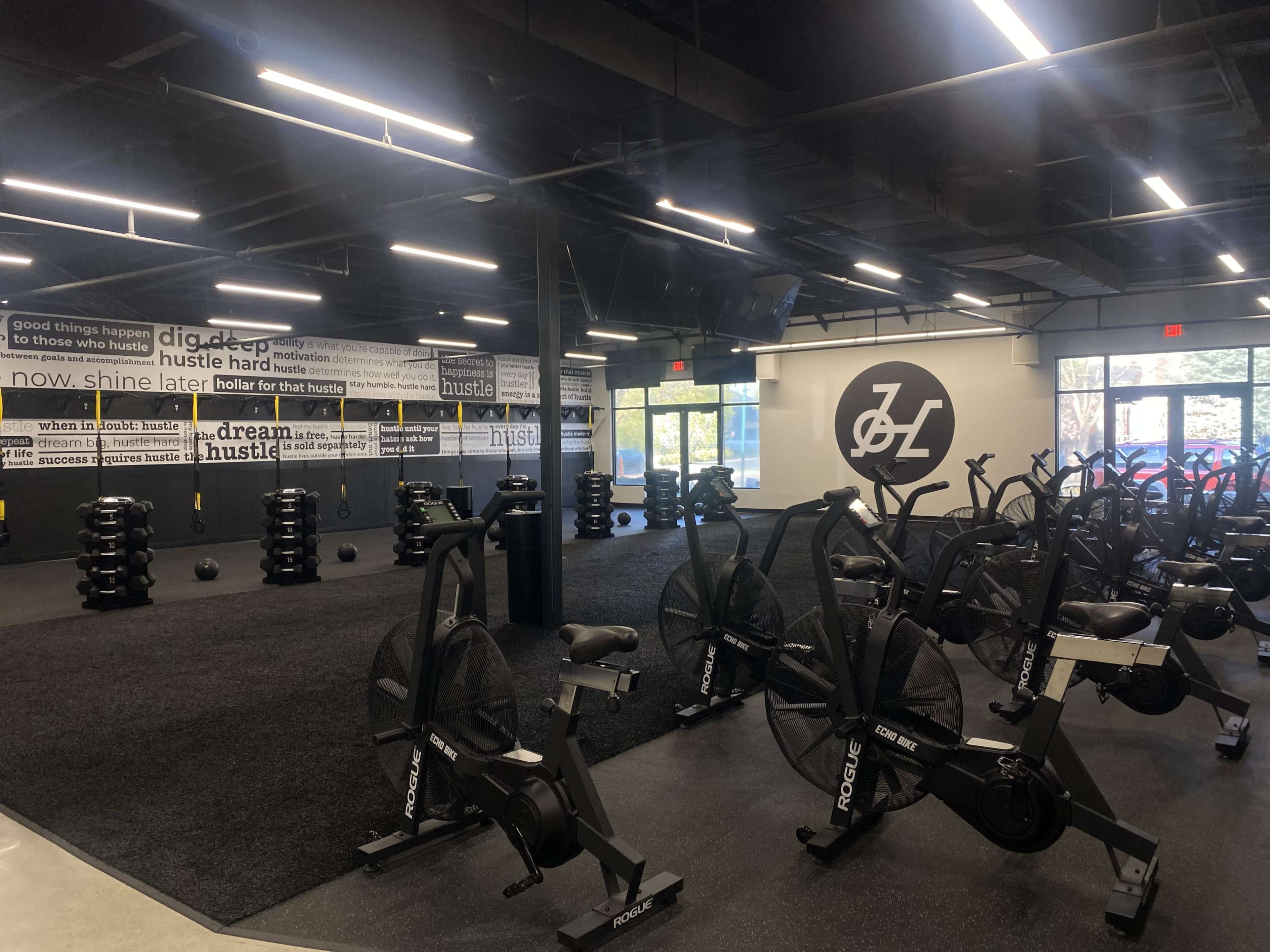 A fitness studio with stationary bikes, weight racks, and motivational wall graphics in a well-lit space.