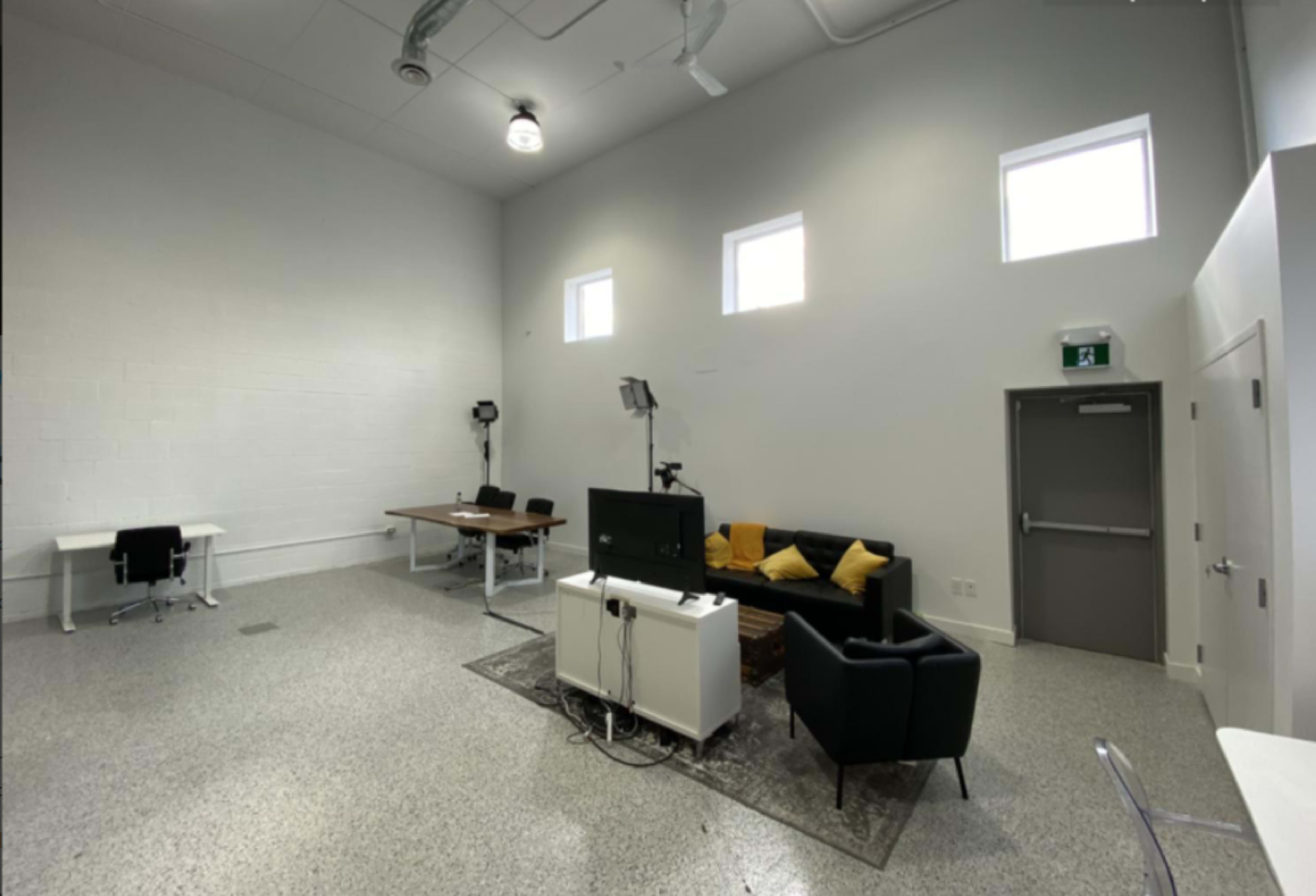 A spacious, minimalistic room with grey walls, a table with chairs, a sofa, and a TV on a stand.
