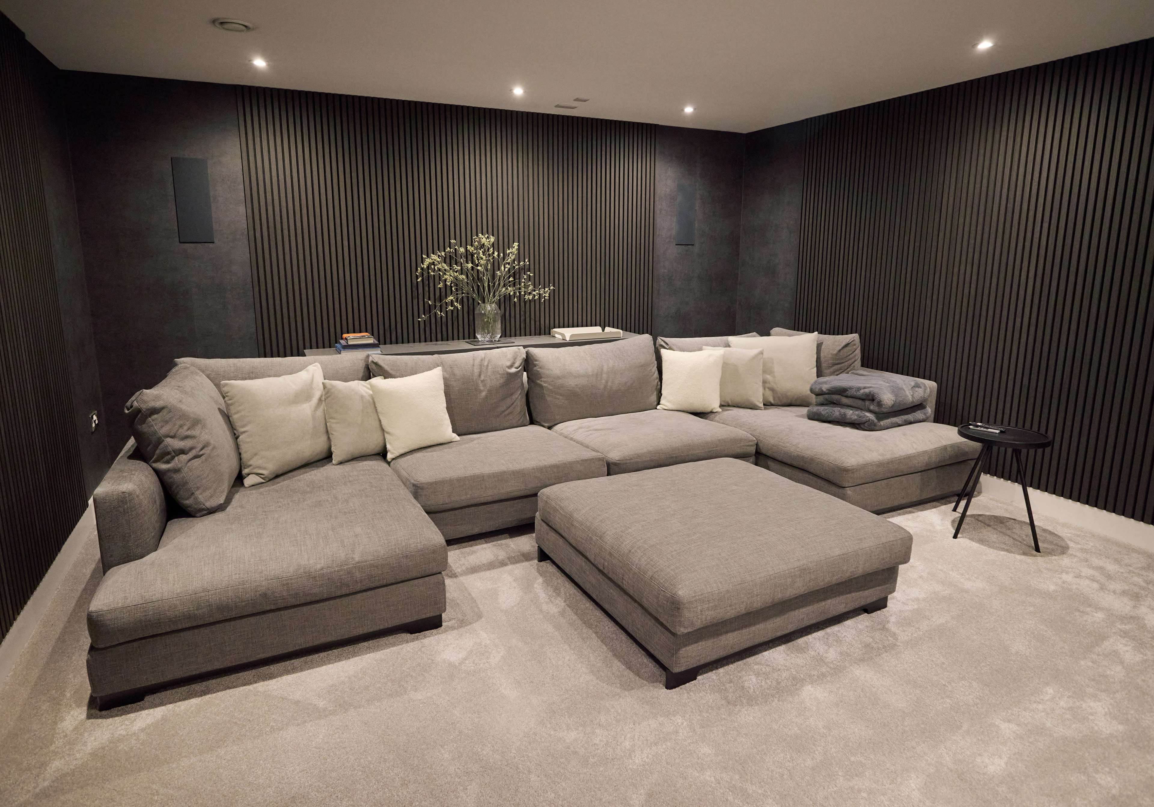 The image shows a modern living room featuring a large gray sectional sofa with multiple cushions, a small black side table, and dark textured walls.